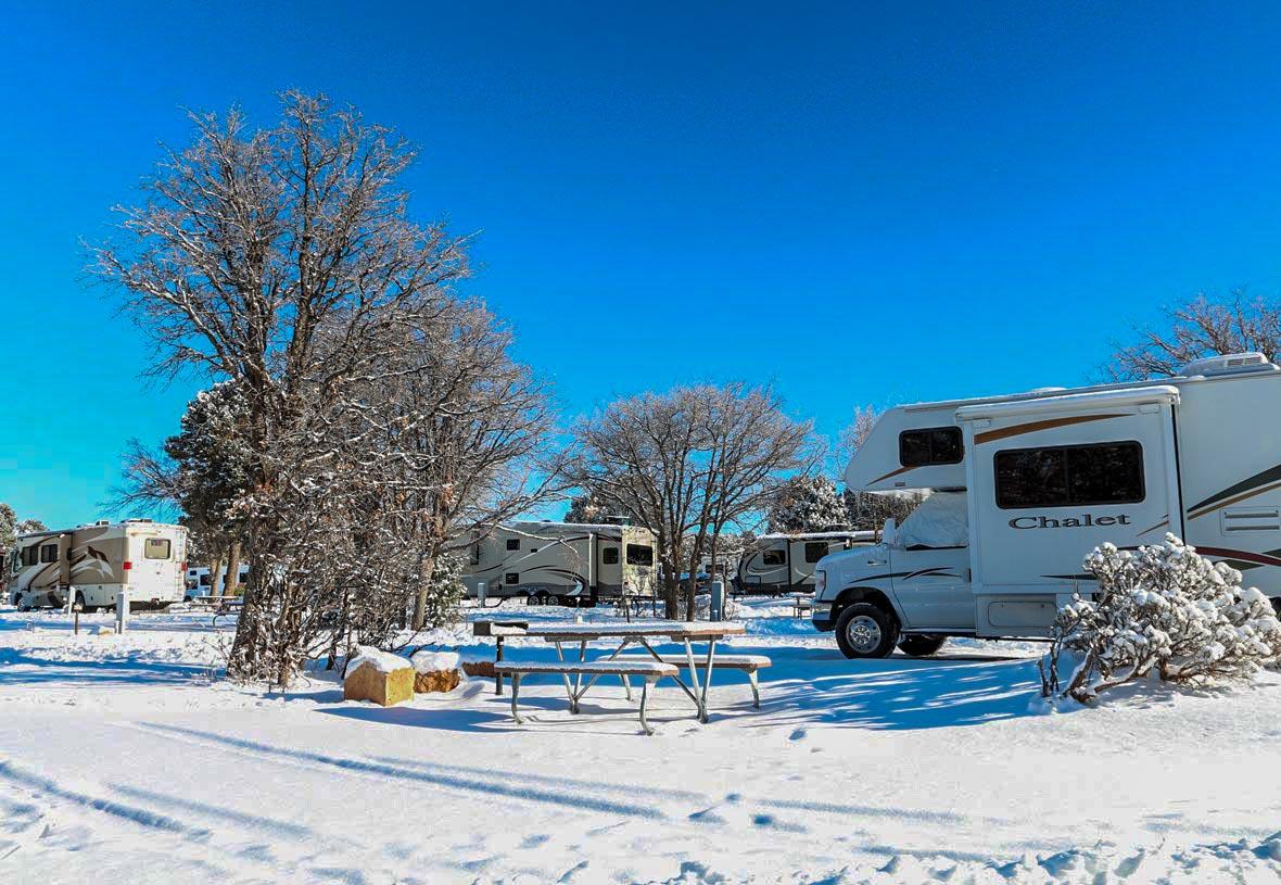 Several RVs parked in individual sites with several inches of snow covering the ground.