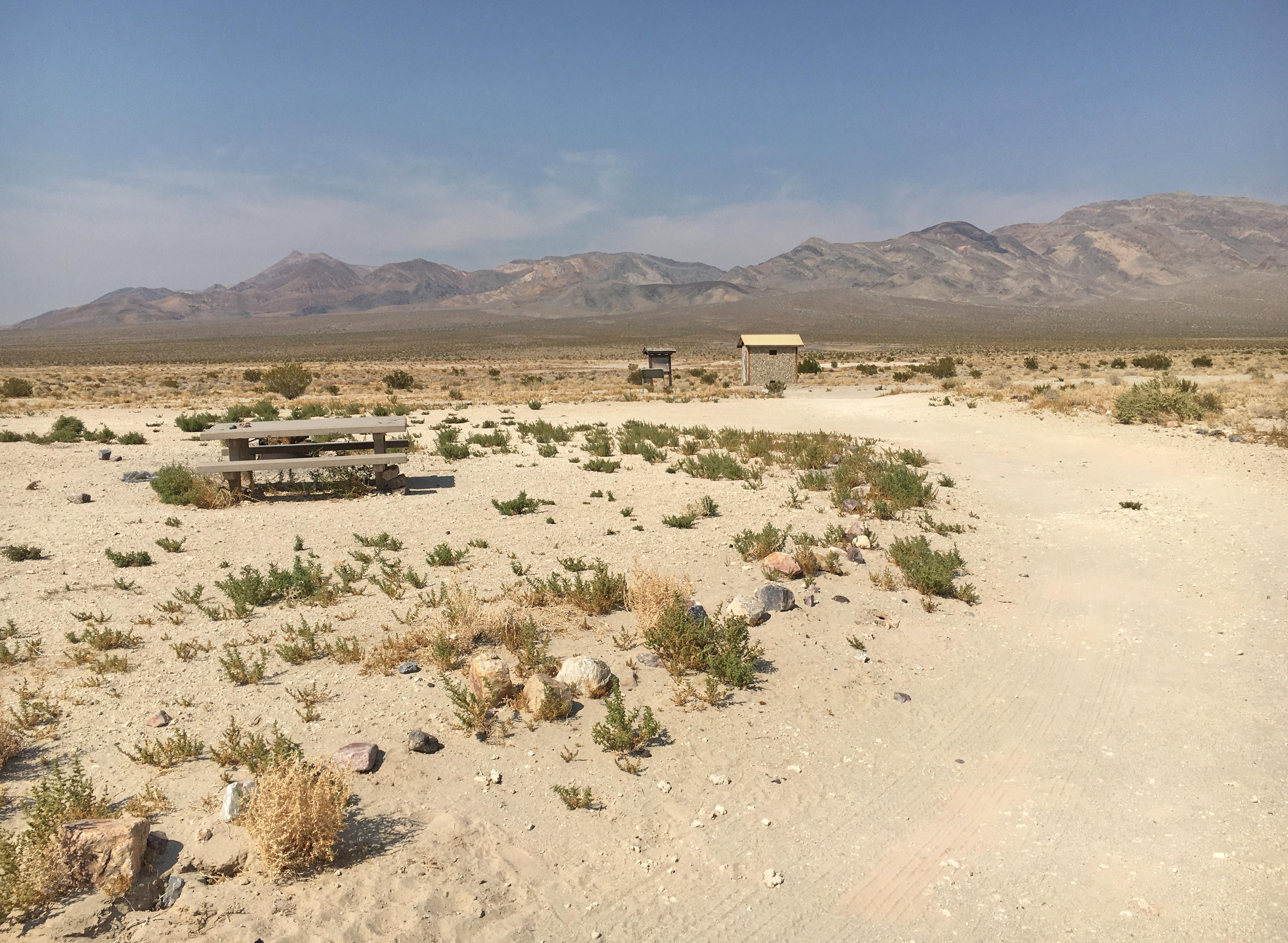 View of the valley, campsite, picnic table and pit toilet from the campground road.