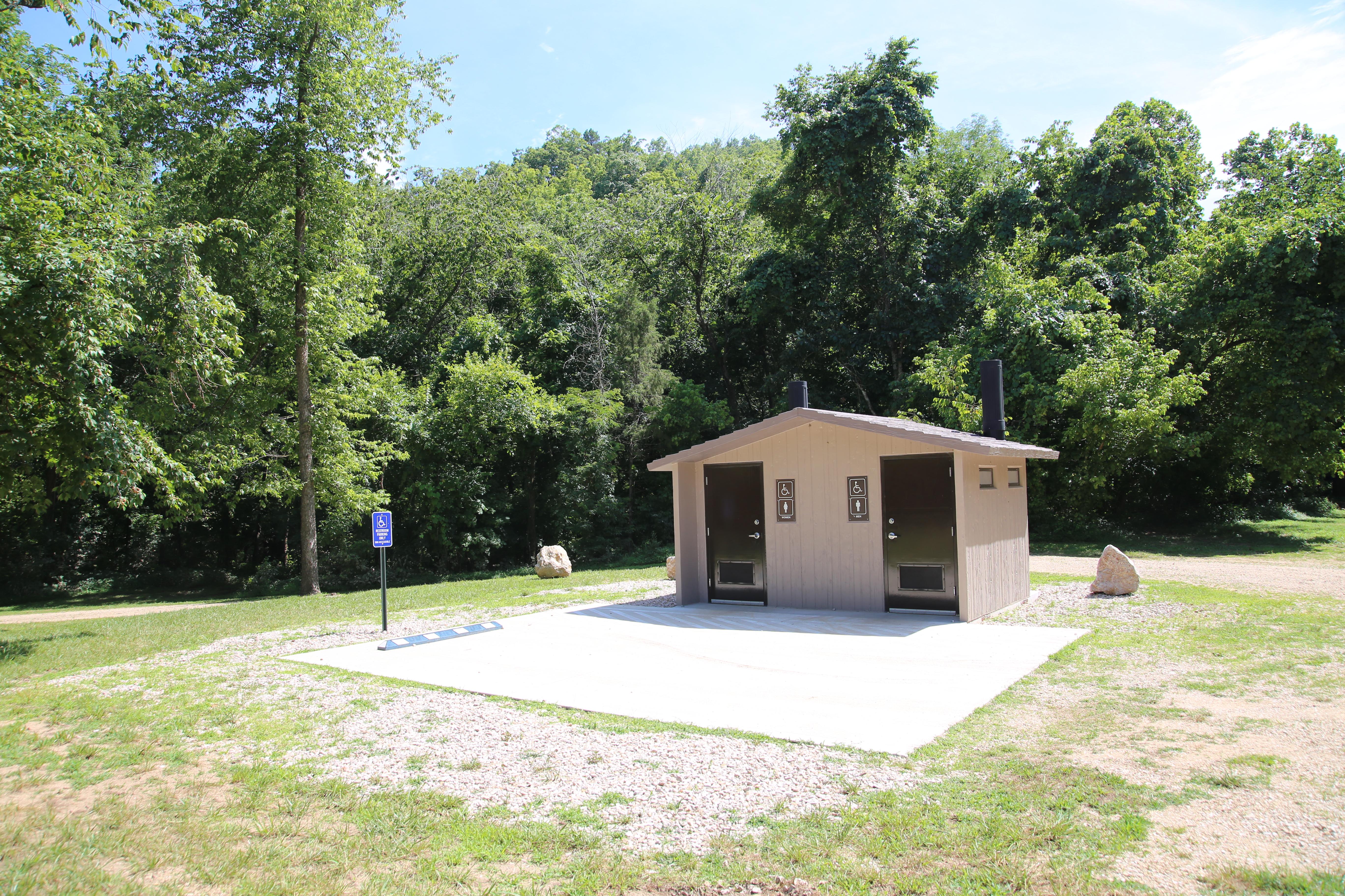 A concrete restroom building next to an accessible parking pad.