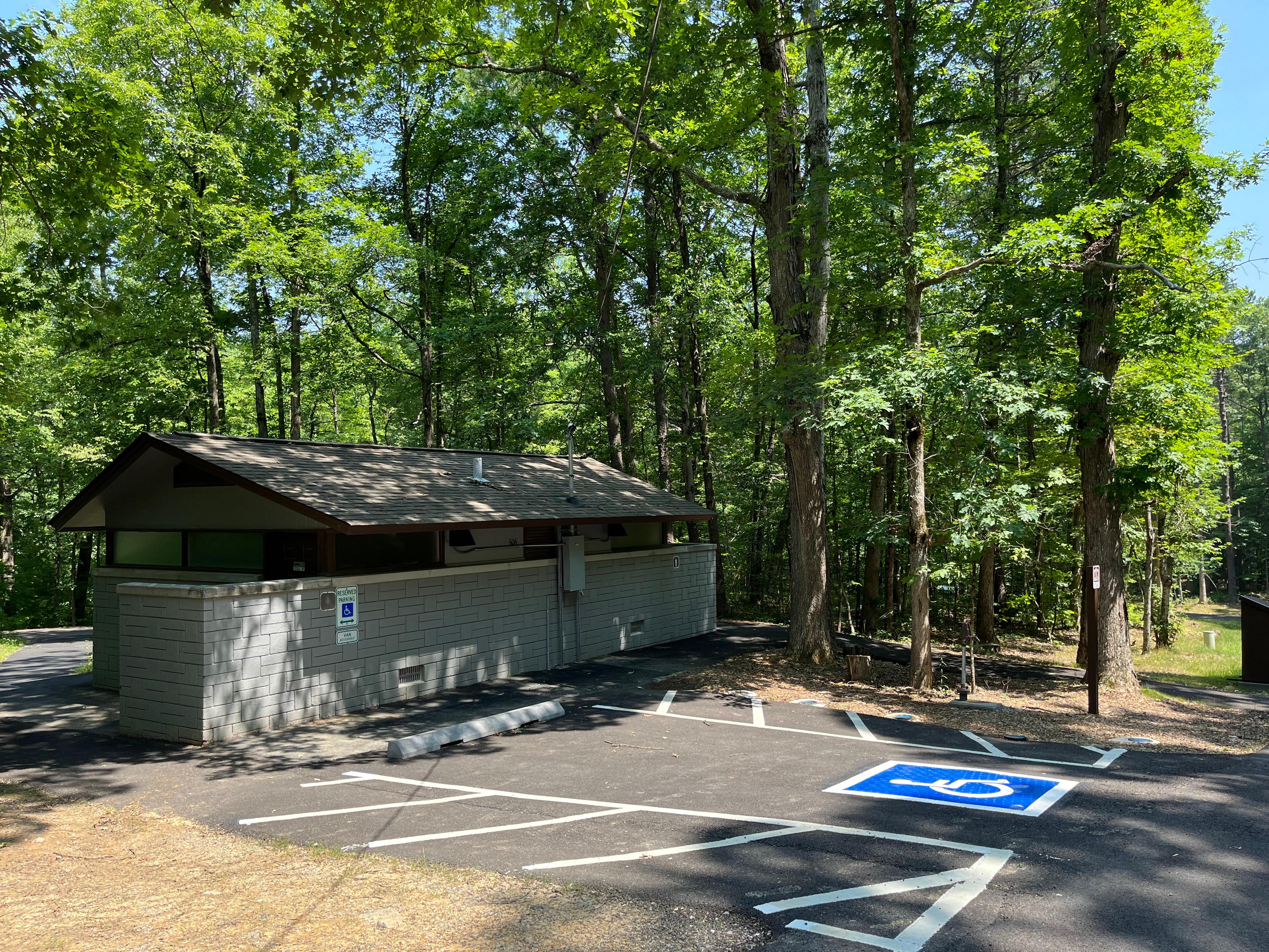 Paved handicap accessible parking beside a restroom facility surrounded by trees.