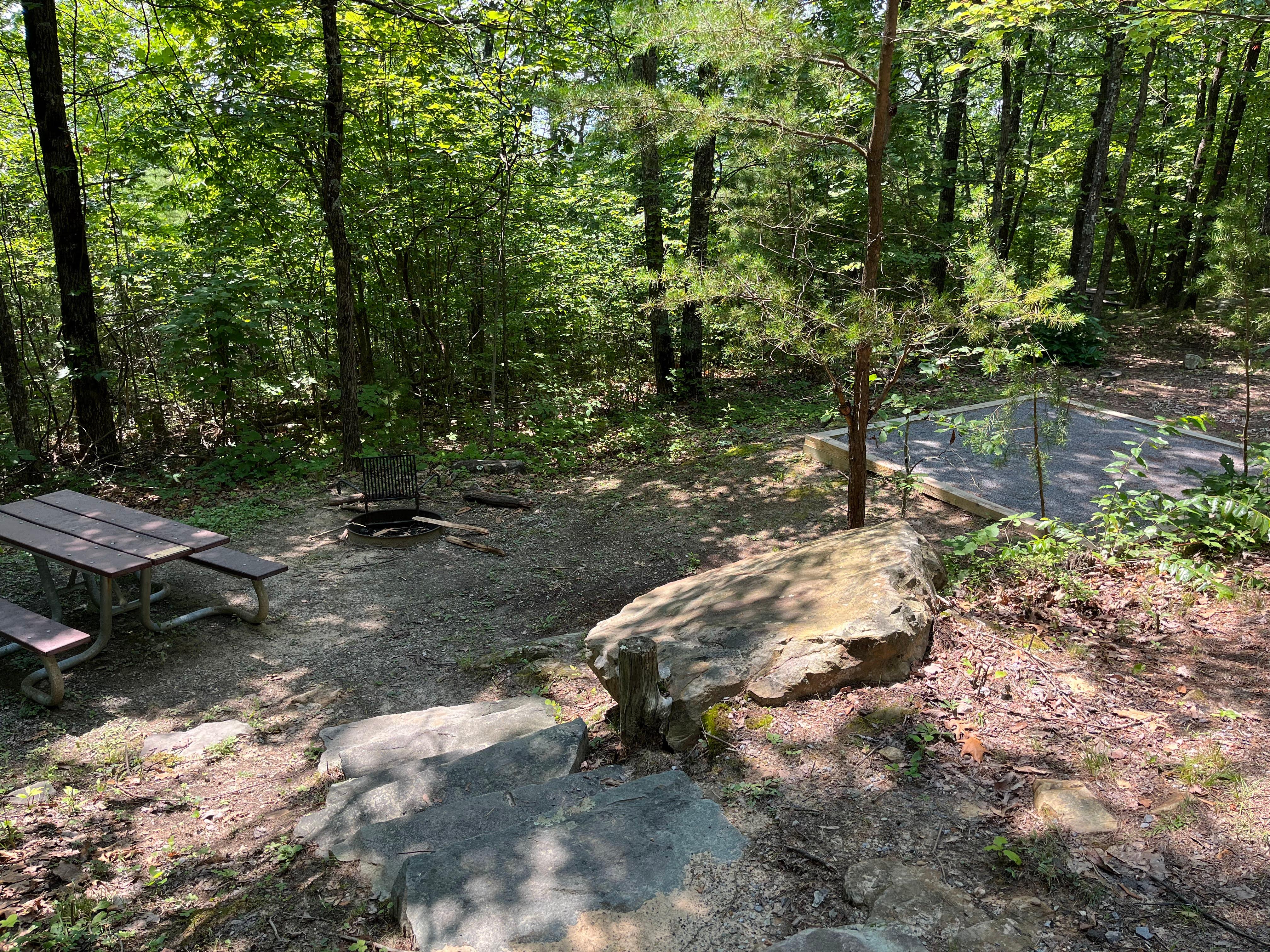 A set of stone stairs leads down to a picnic table, fire ring, and gravel tent pad.