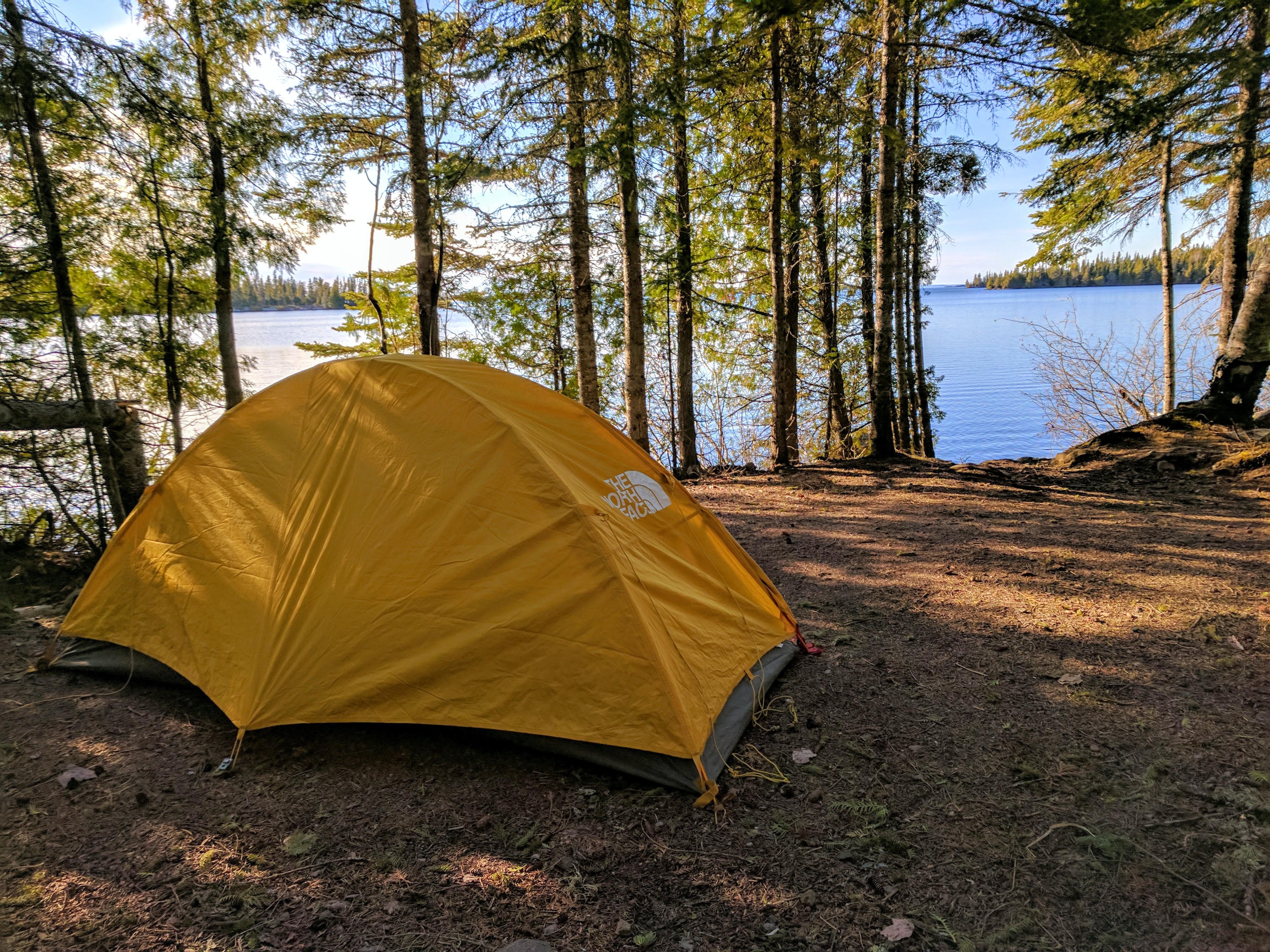 Yellow Tent in a campsite along Lake Superior with trees along the shoreline.