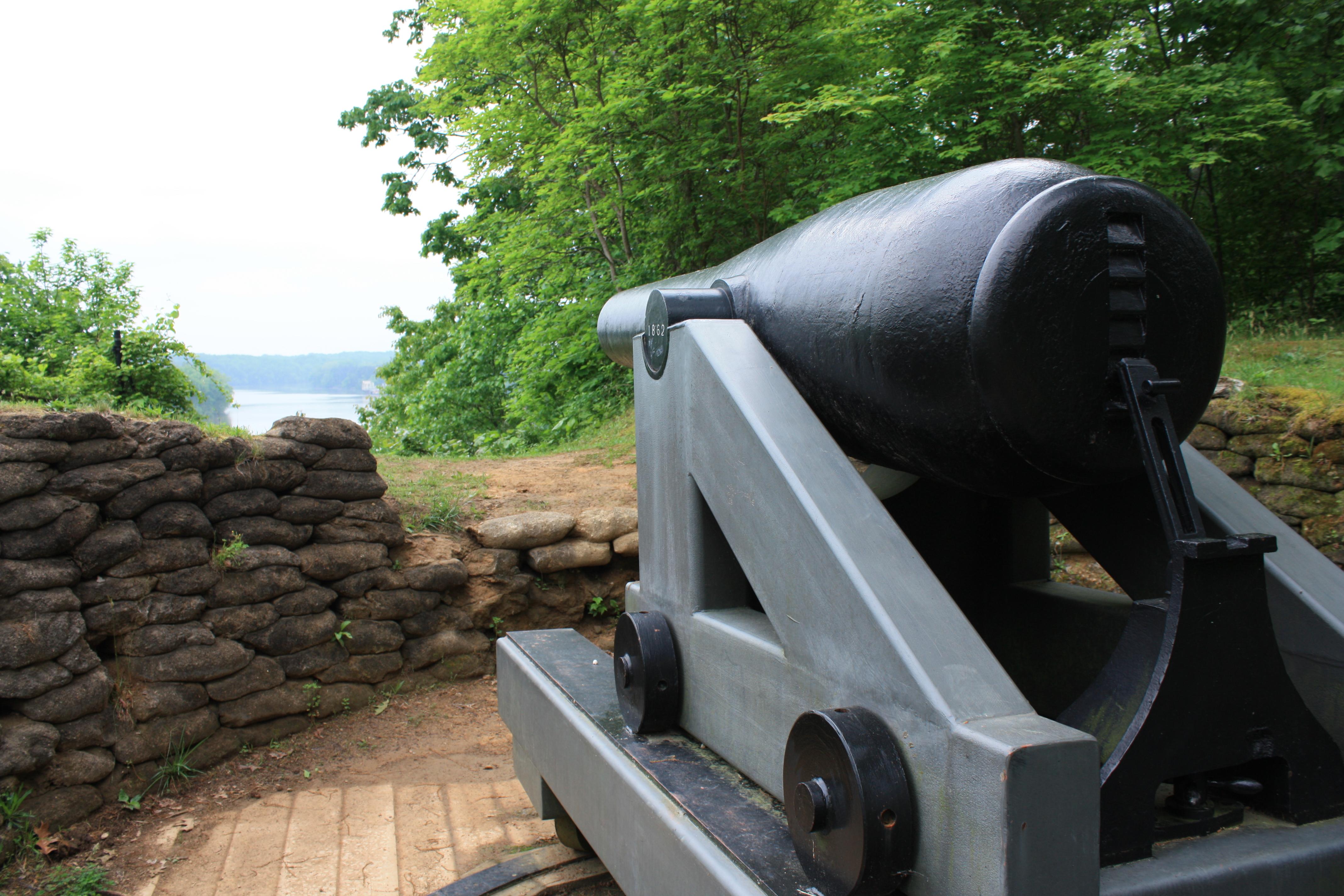 A large, black Civil War cannon overlooking a river from a high bluff.