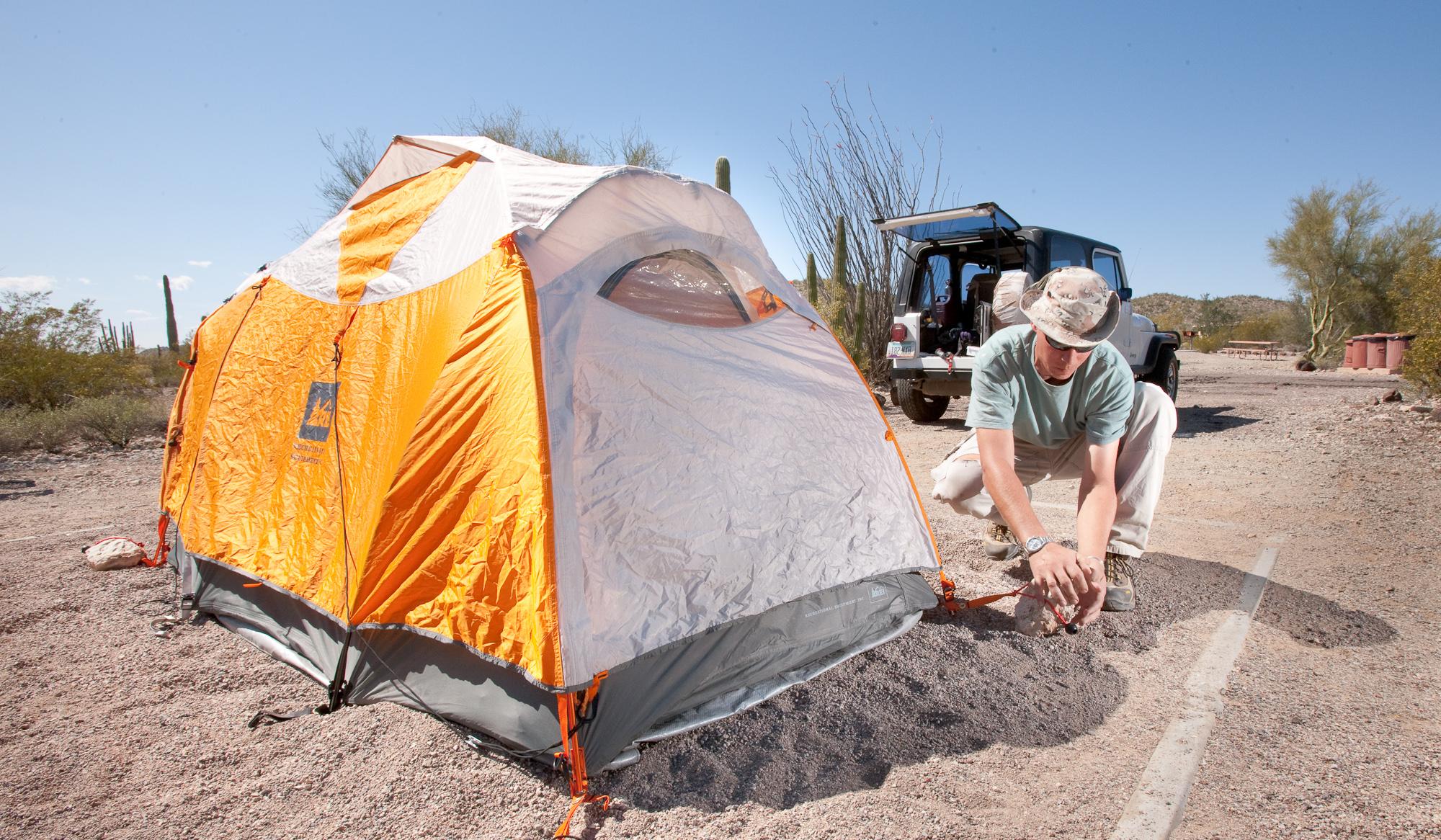 man putting up an orange tent on a gravel tent pad in the desert
