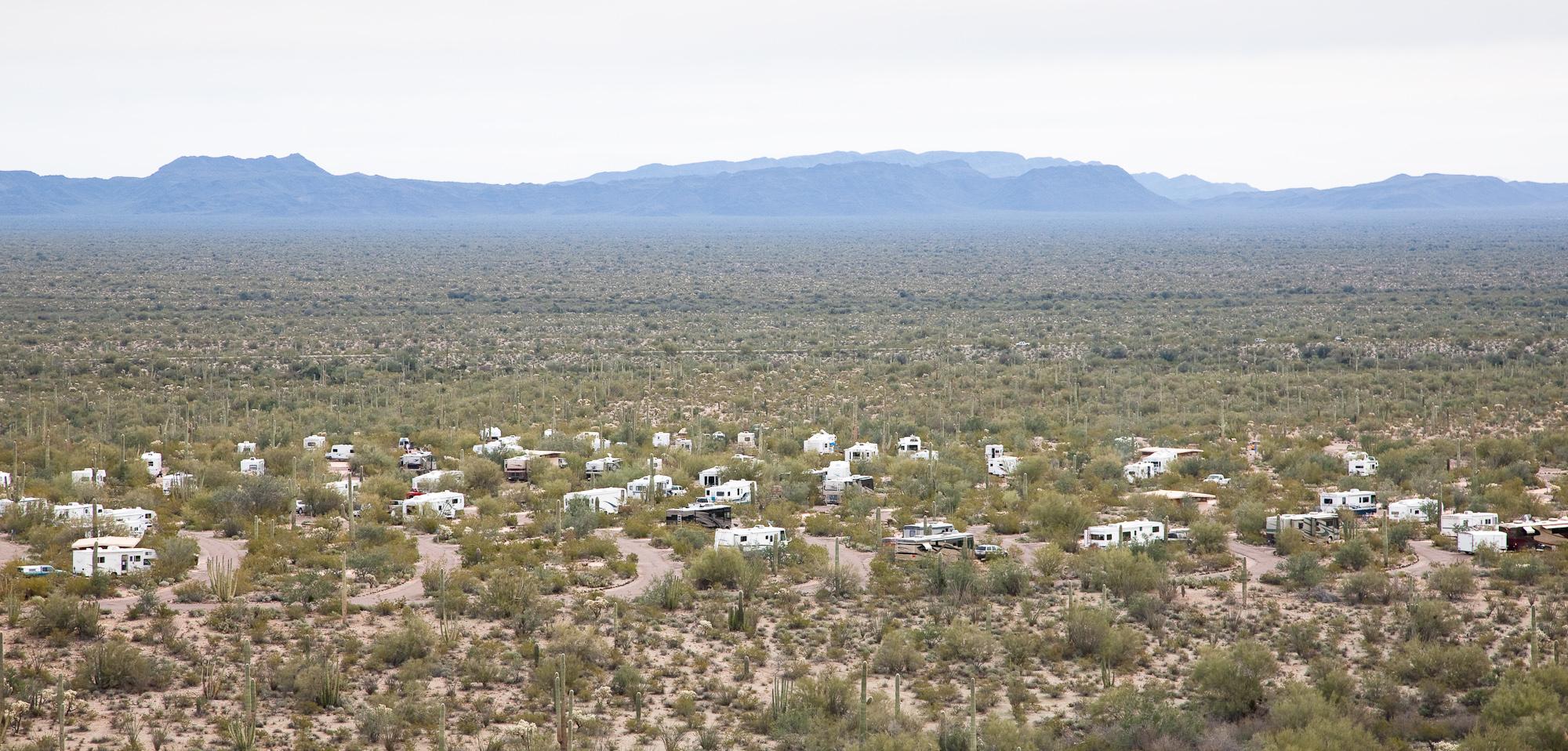 View of many RVs in campground, surrounded by desert landscape with mountains in the distance