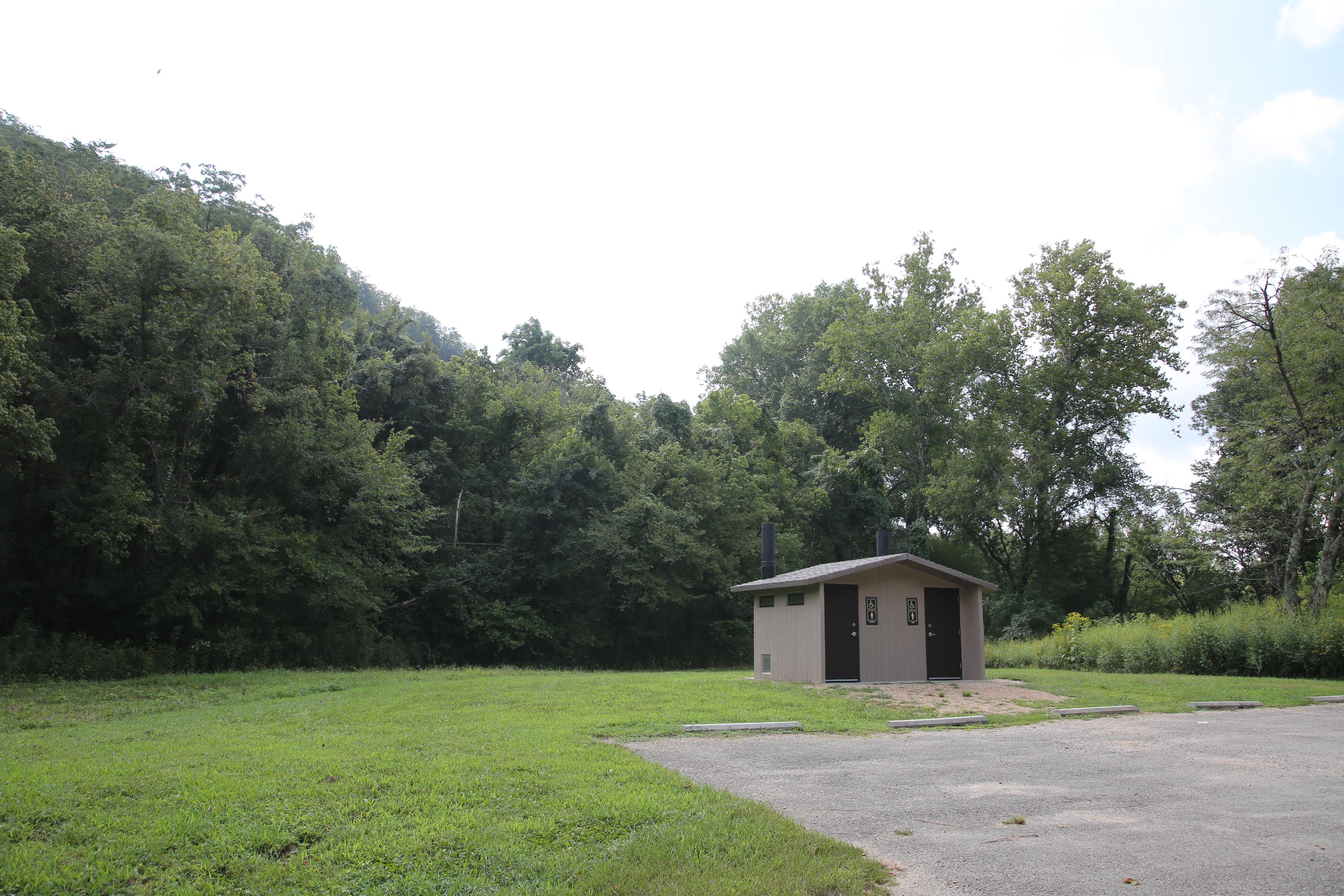 A small concrete restroom building with woods in the background.