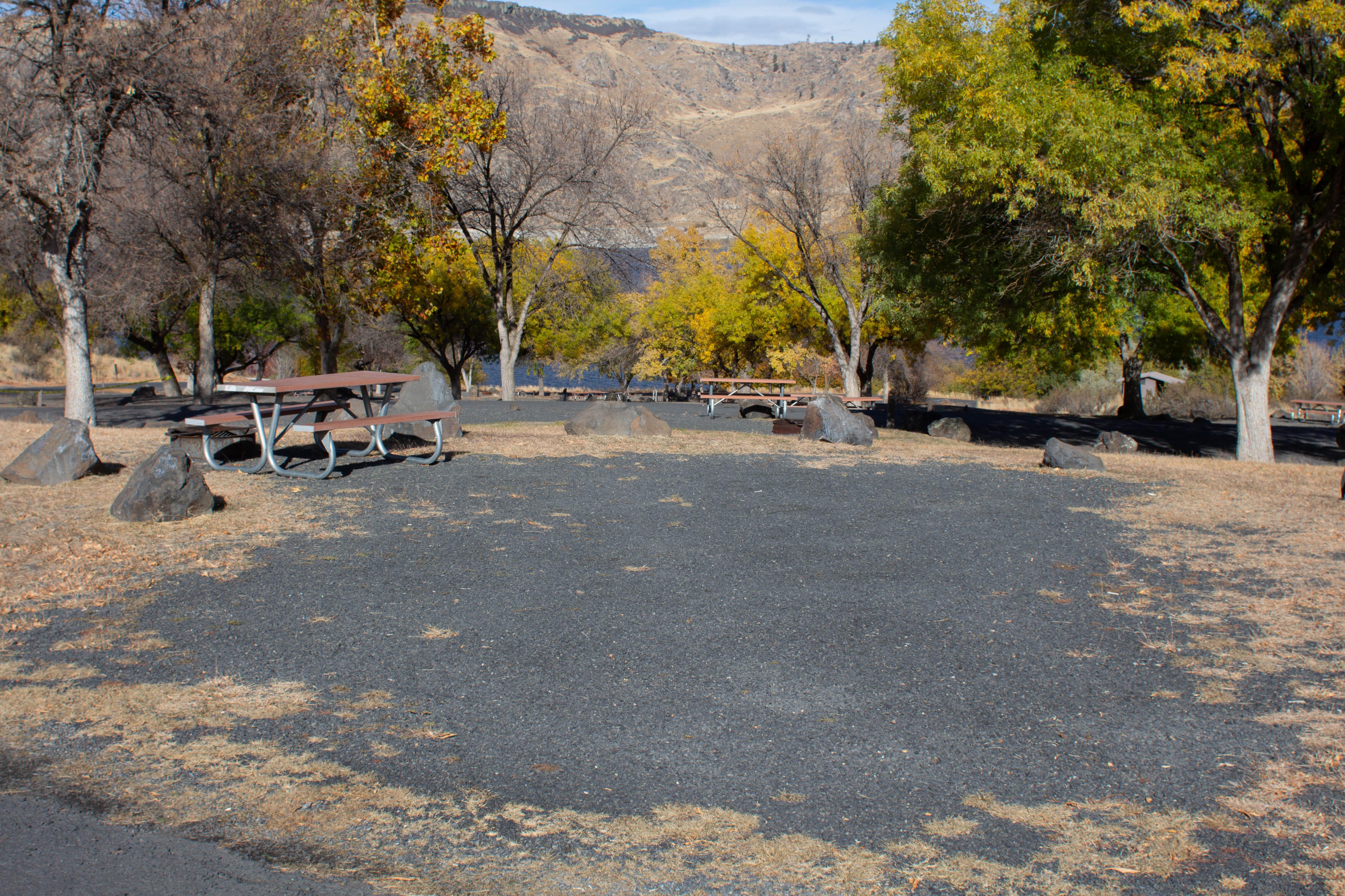 A wide grey gravel parking area is adjacent to a brown and silver picnic bench.