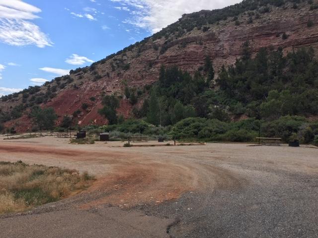 A gravel road with several well spaced out camp spots along a red rock background.