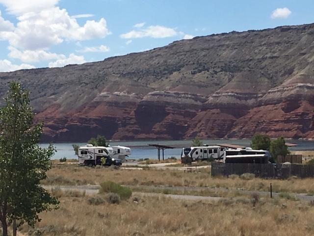 Several despersed camp sites on an open desert plain with the lake and red cliffs in the background.