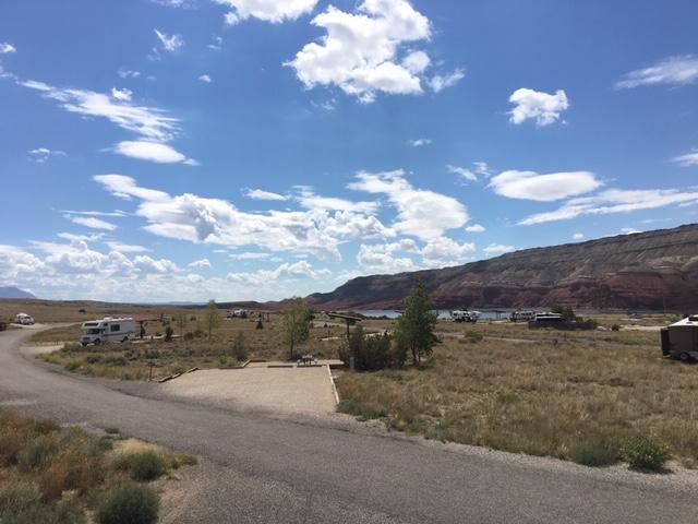 A paved road with gravel campsites disperse in a dessert plain with bright blue sky and a few clouds