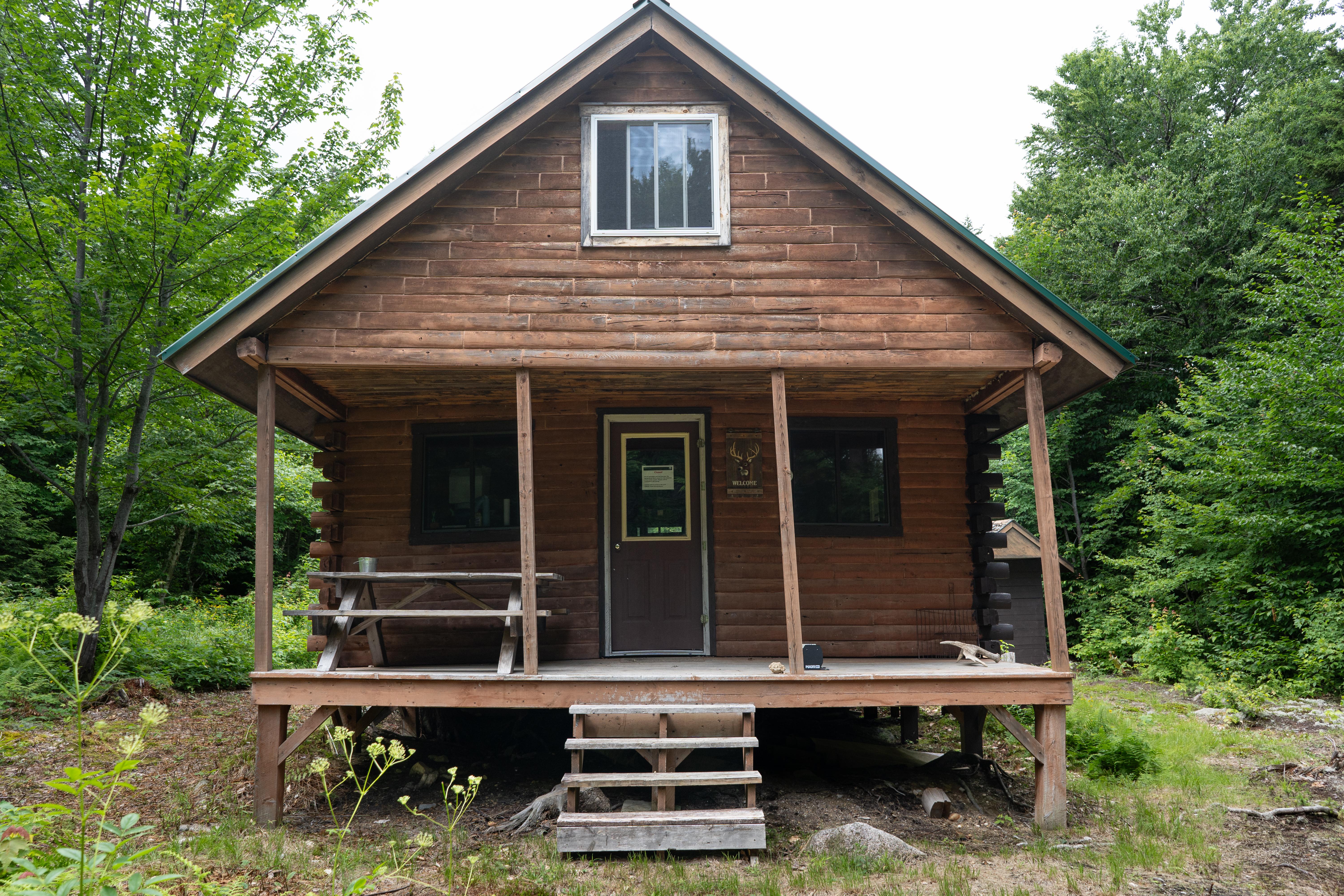 The front of a log cabin with a porch and steps in the woods.
