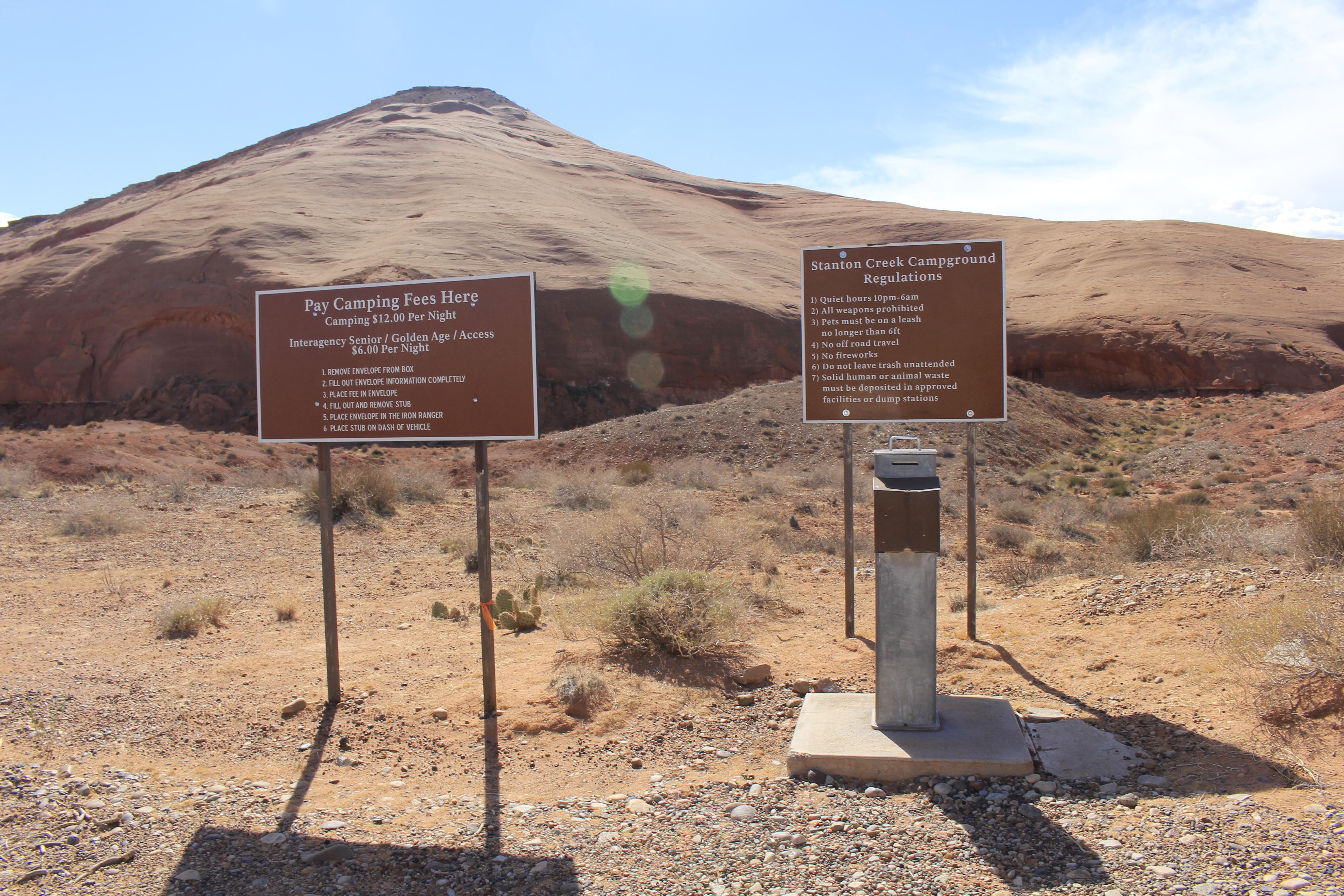 Two signs describing campground fees and regulations above an iron post.