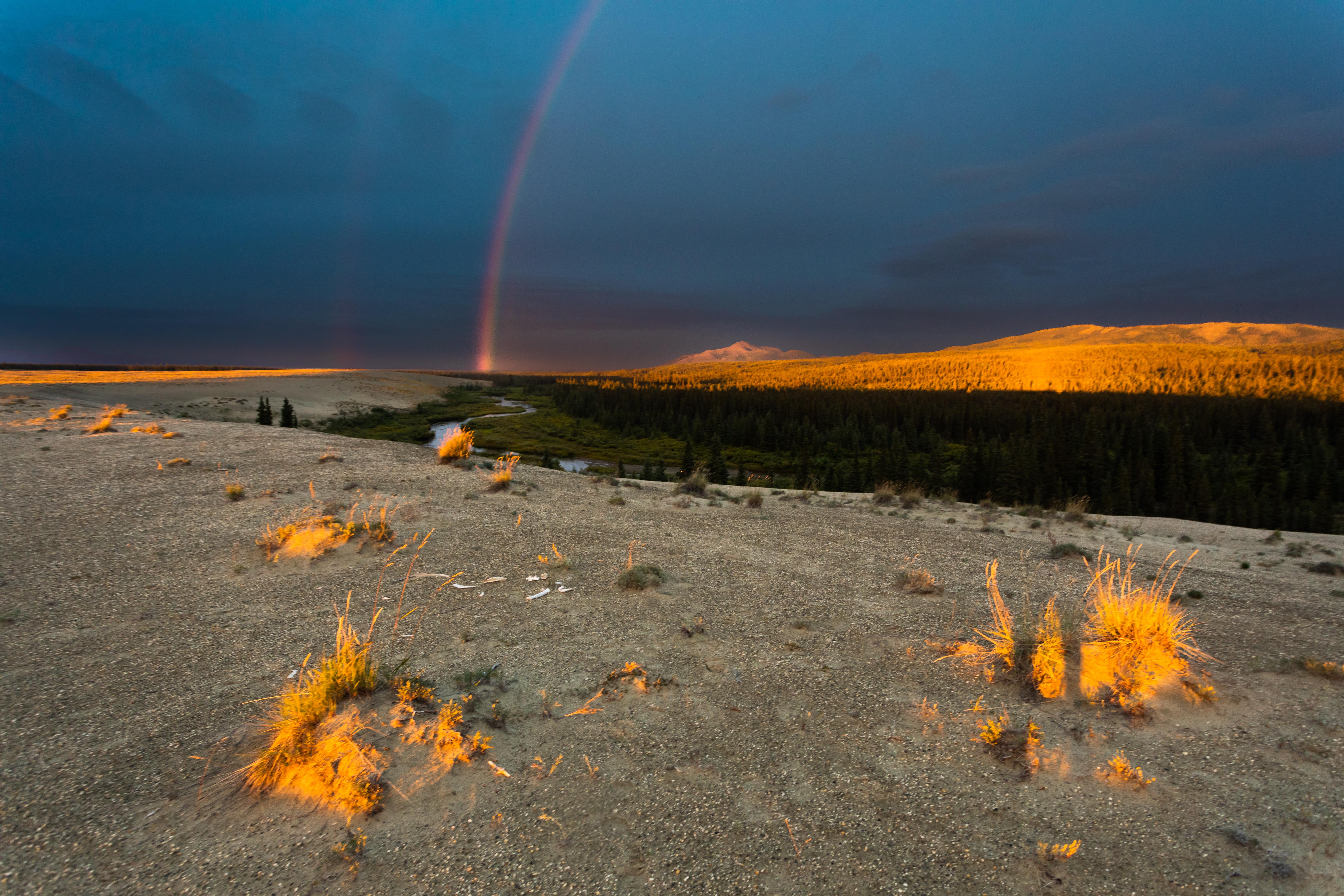 Dark skies shadow the horizon. A rainbow is illuminated above Niaktovik Creek