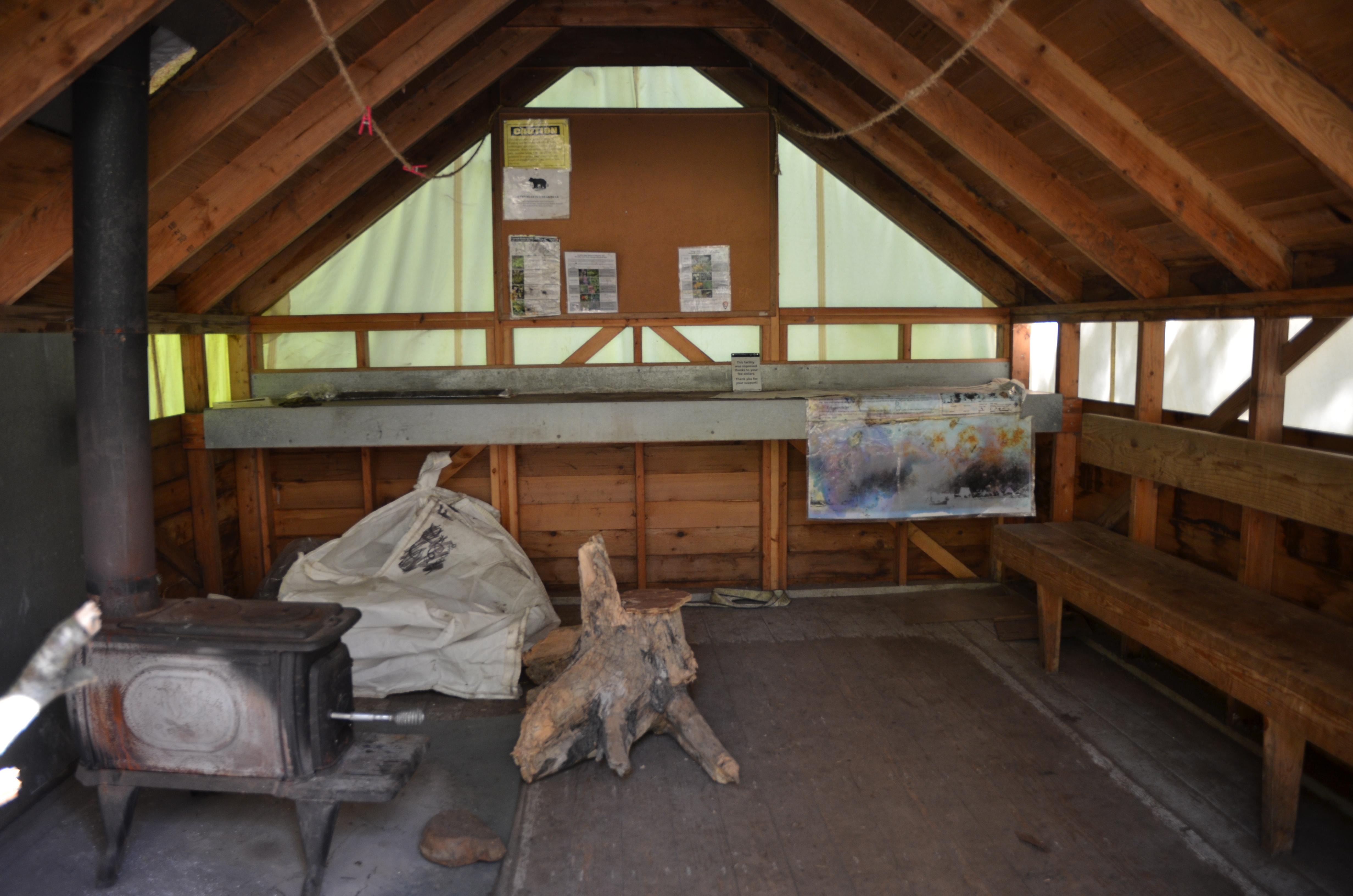 Inside of a small framed structure.  Benches along the wall and cast iron stove.