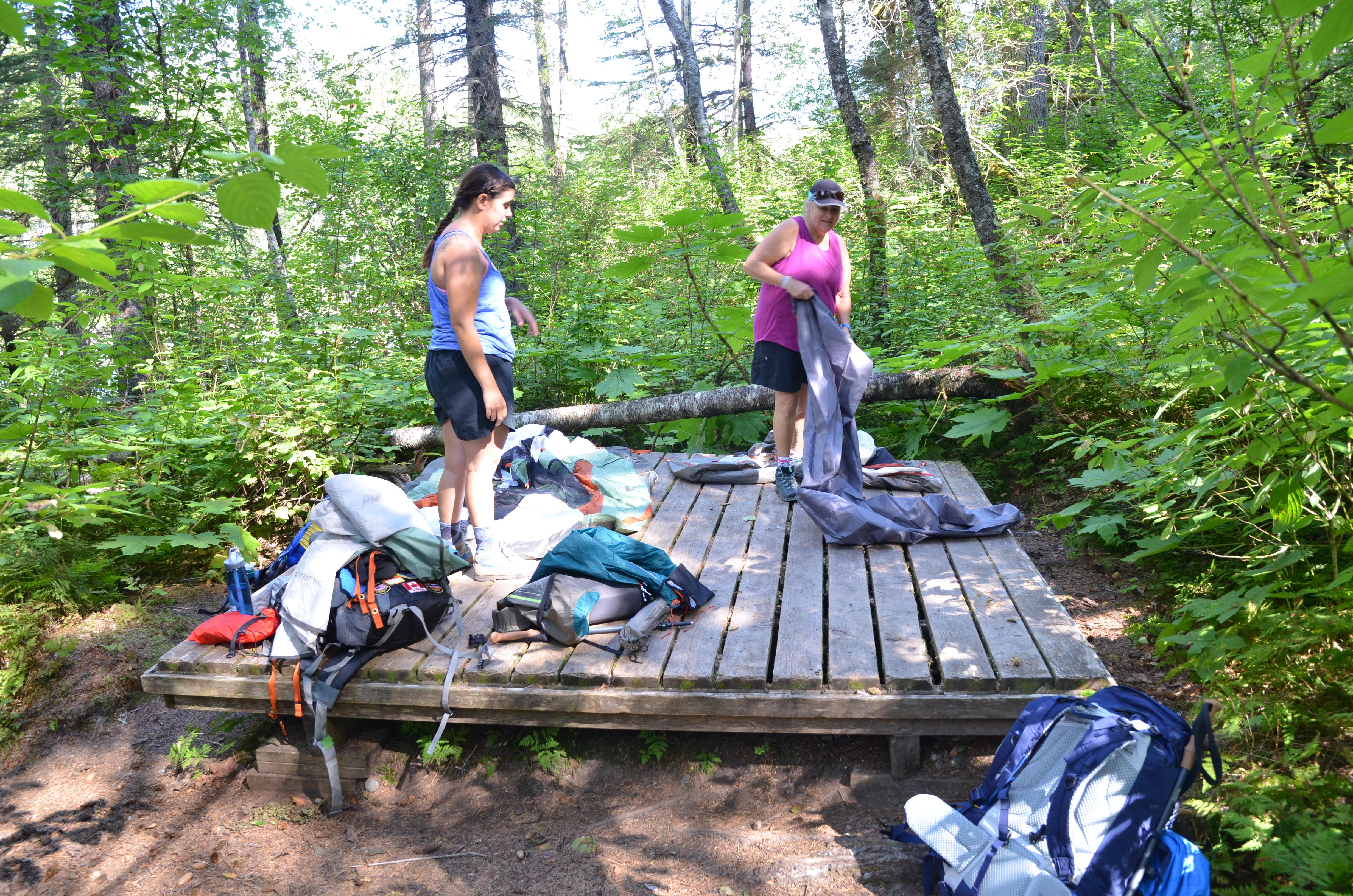 Two women with backpacking gear stand on a large wooden platform