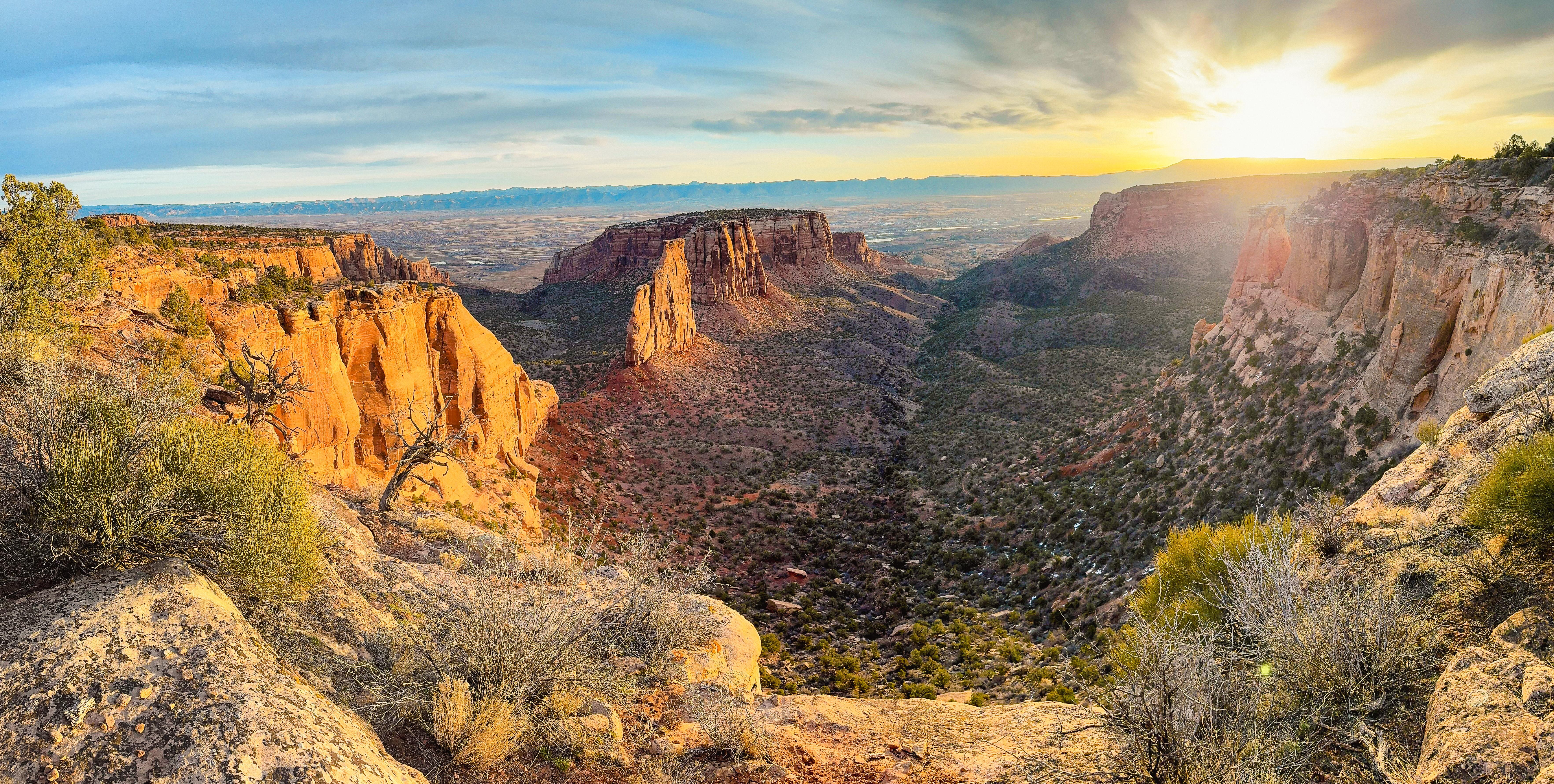 red-orange cliffs frame rolling green canyon bottoms at sunrise