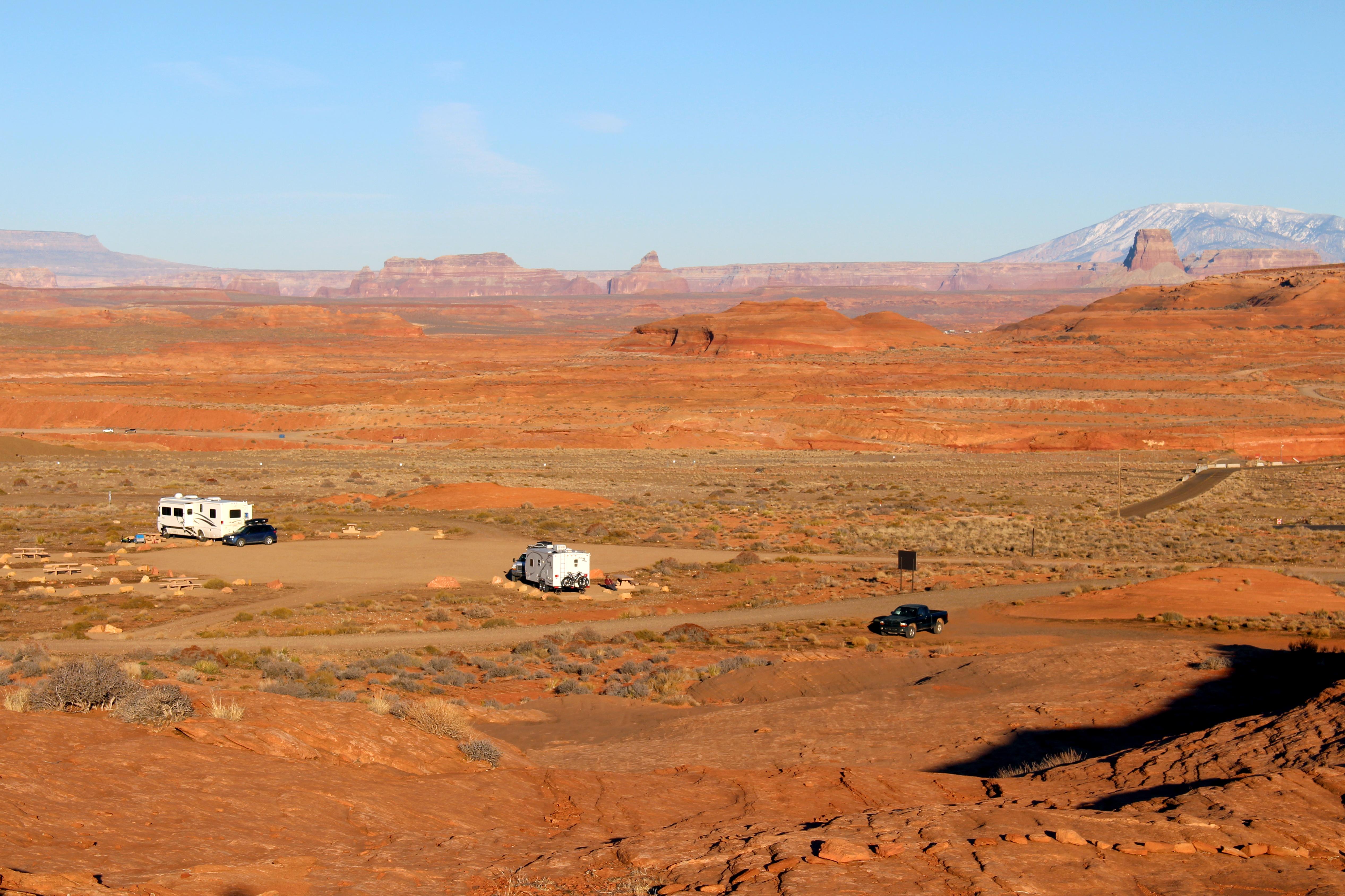 Two RVs and a black truck on rugged road. Mountain and cliffs in background.