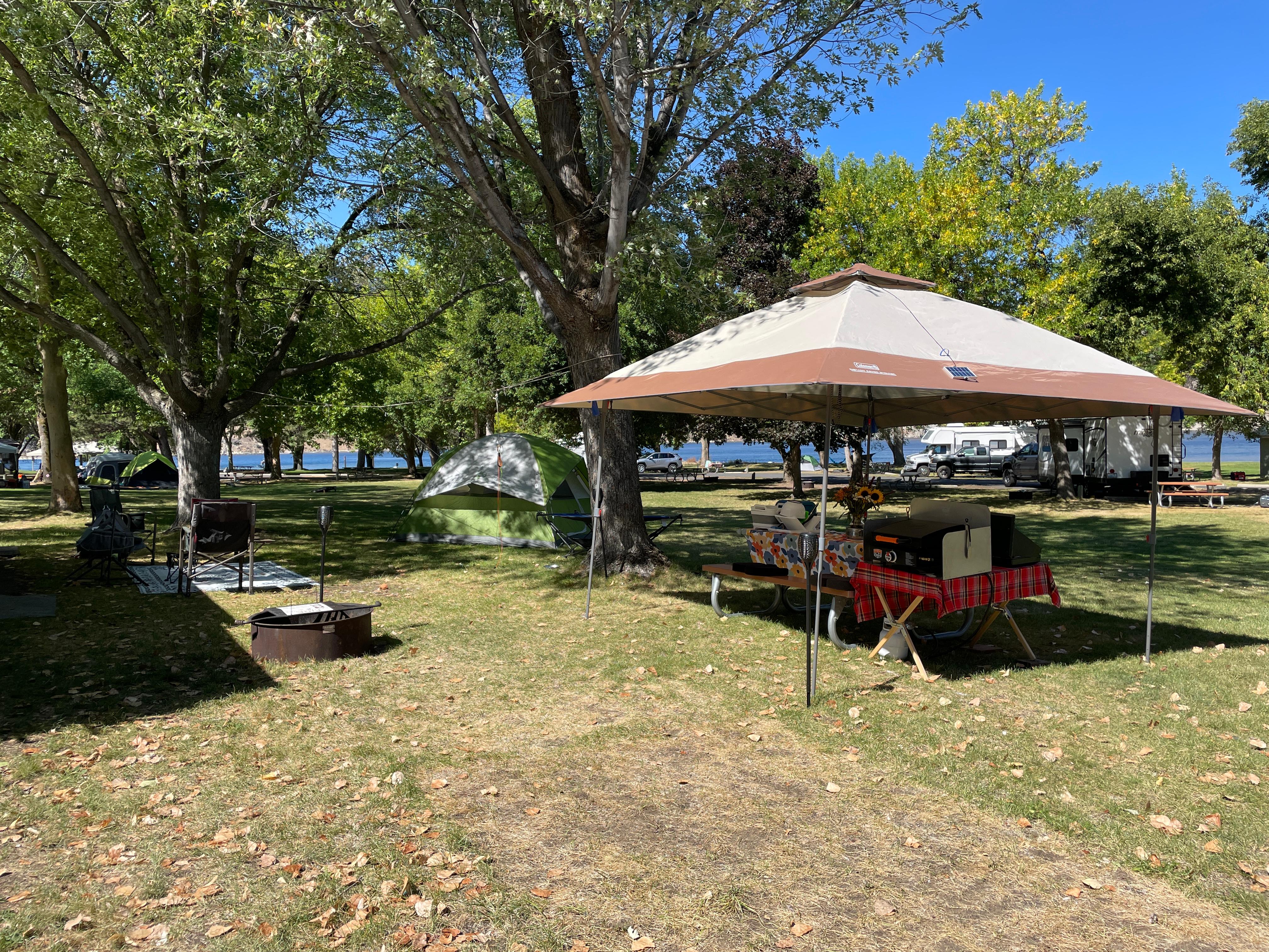 Large tents and shade structures are spread out on grass surrounded by green trees.