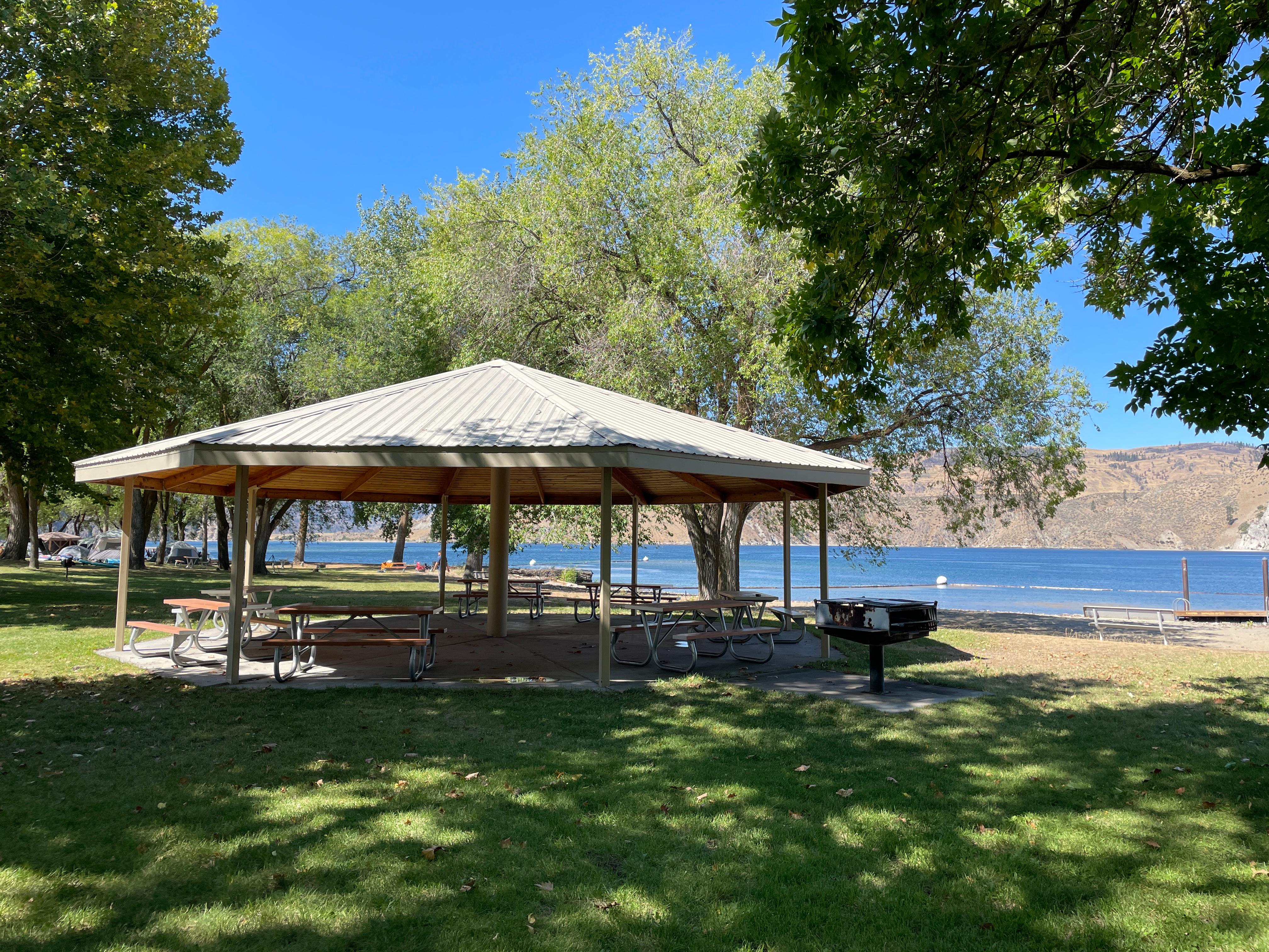 Peaked octagonal shaped structure provides shade for picnic benches.