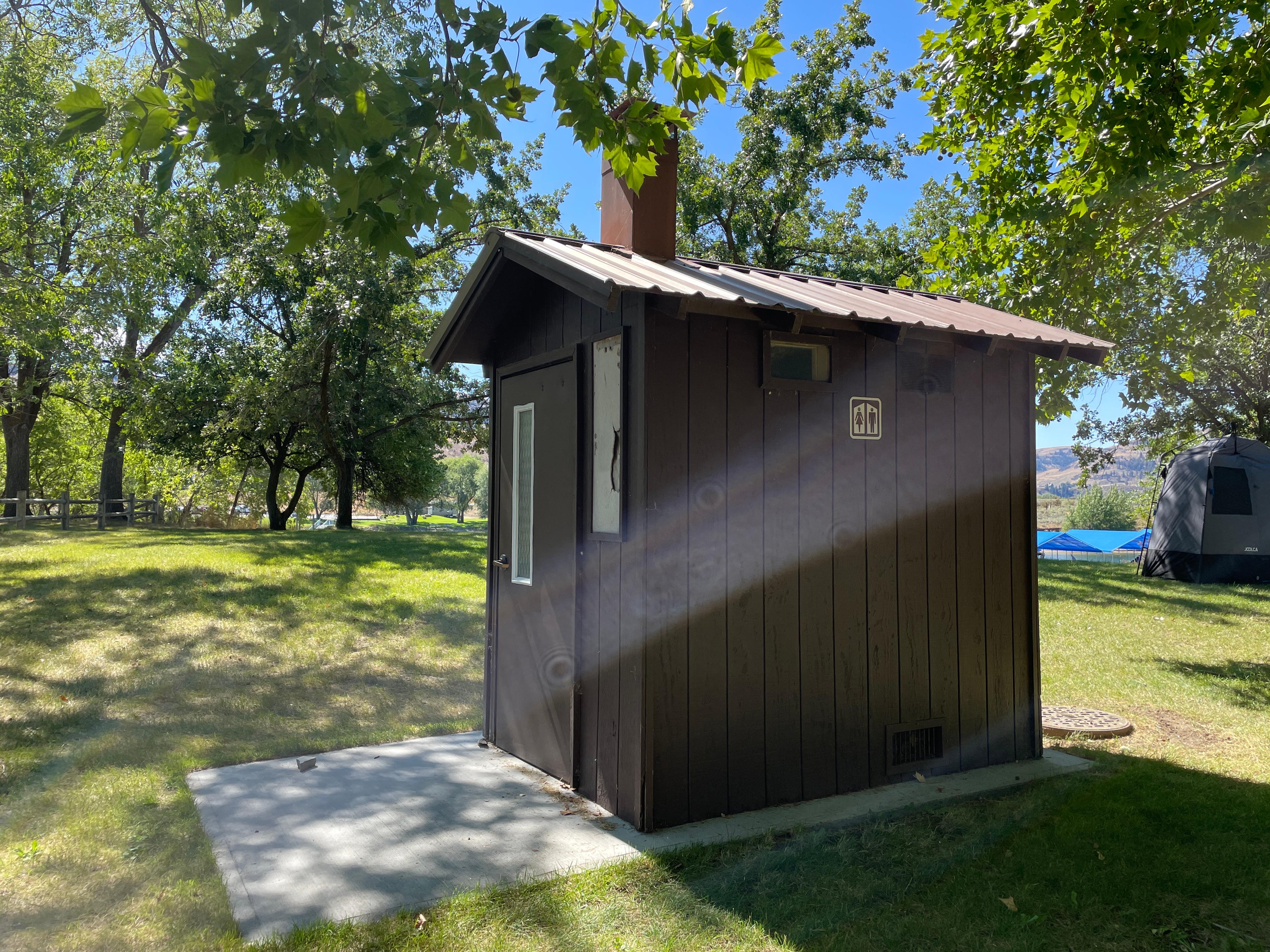 Brown outhouse on asphalt with grass surrounding it.