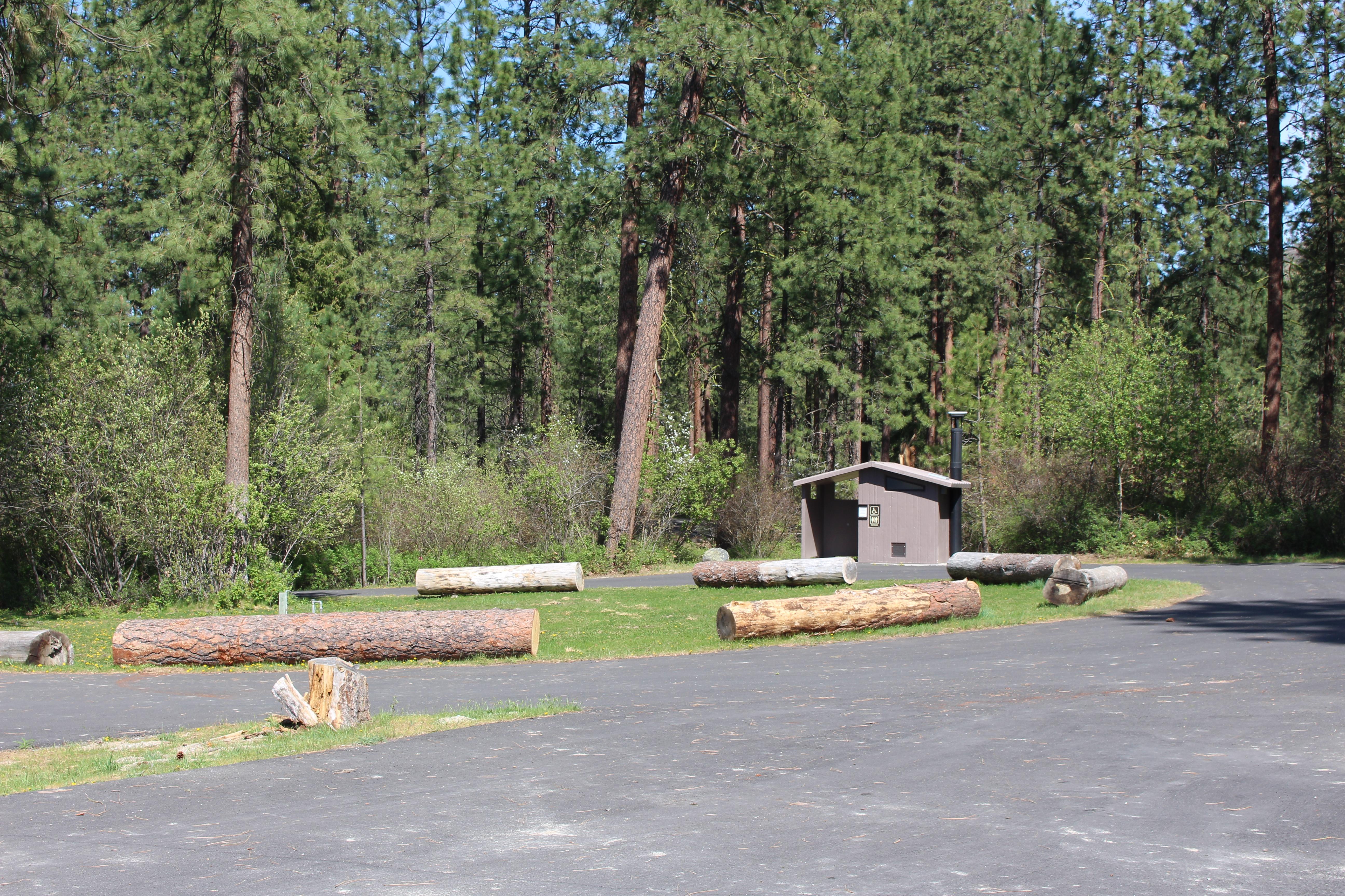 Paved parking areas, log grass bumpers, and an accessible vault toilet building beyond.