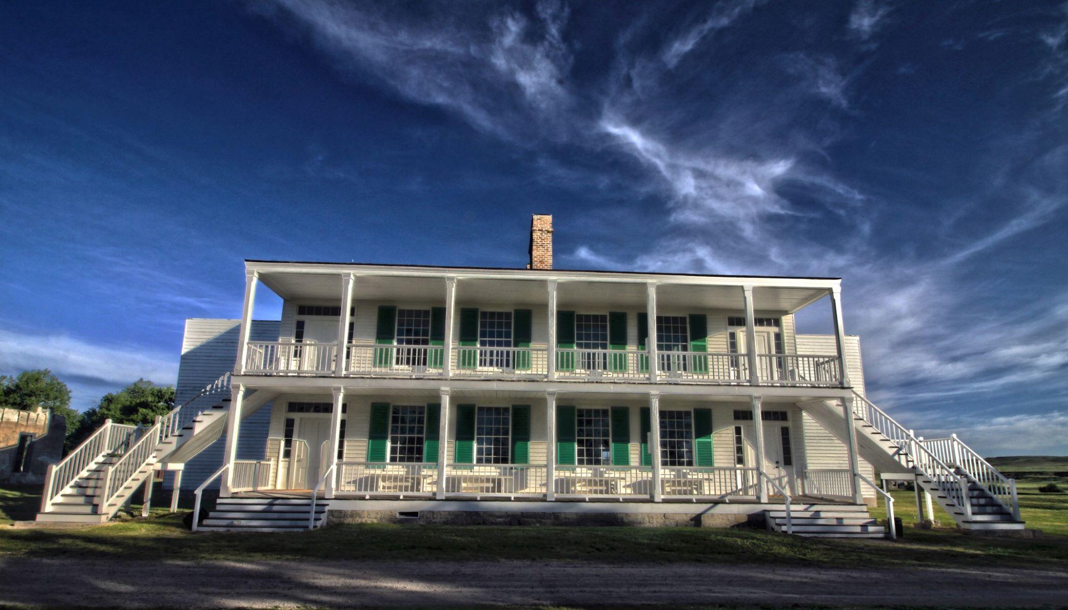 A large two story white building with pillars. Several windows with green shutters