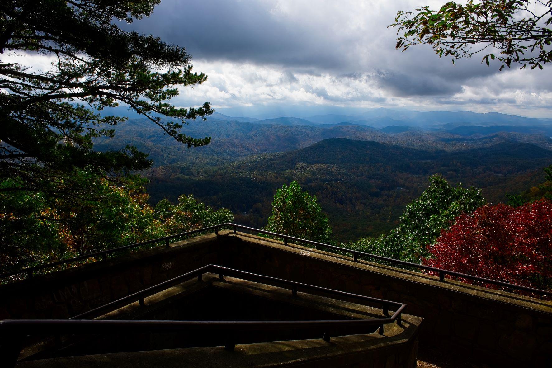 Rolling mountains in early fall under clouds, seen from a viewing platform with a rail.