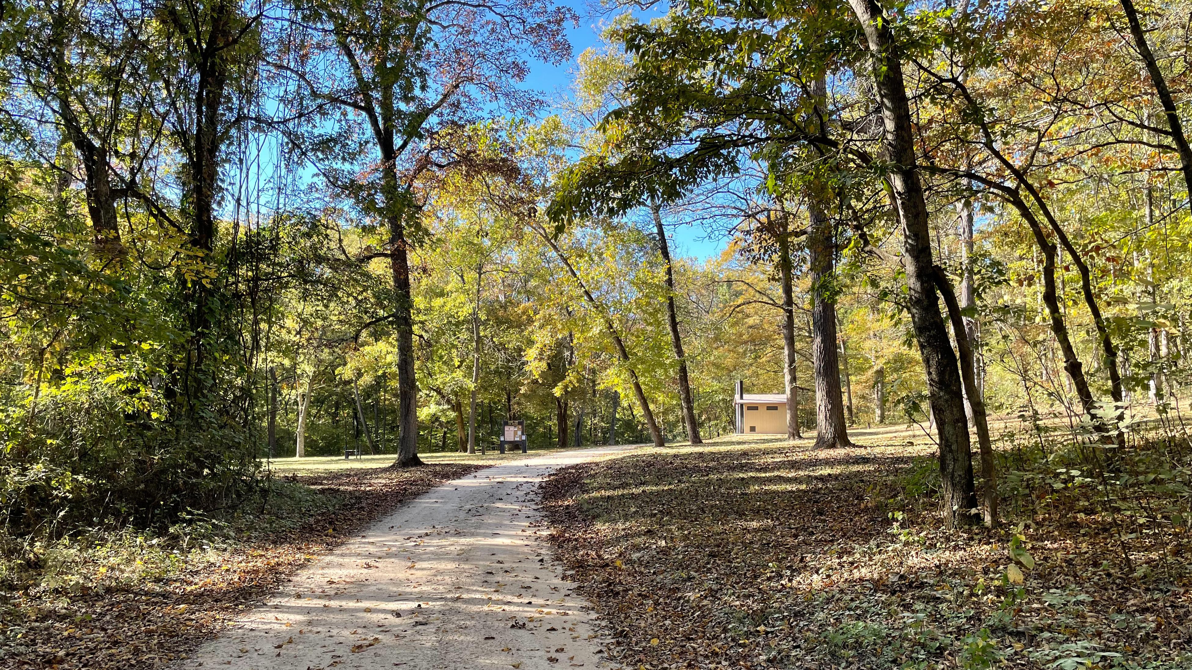 A campground entrance with a gravel road and grassy fields.