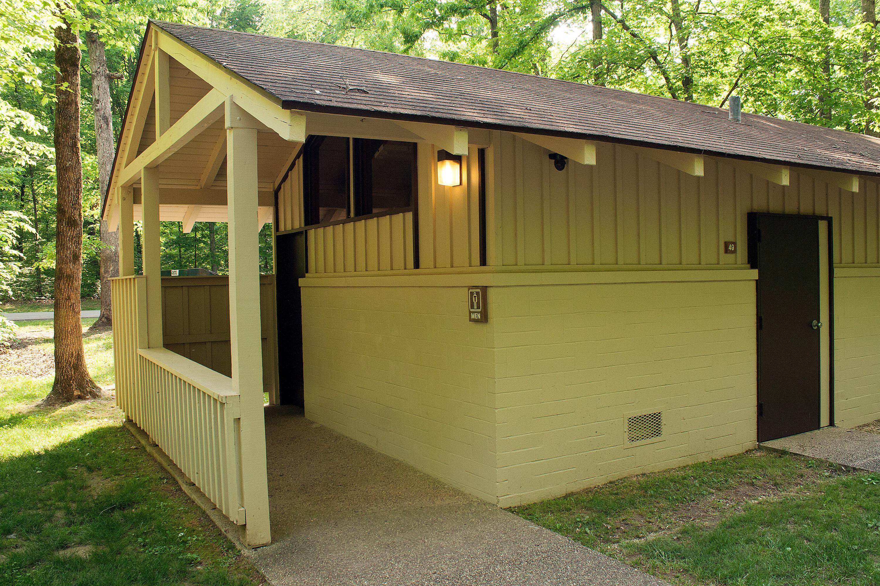 A roofed wooden restroom facility shown from outside.
