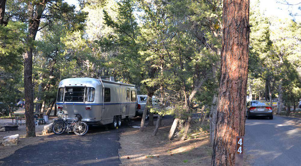 <img alt="Image: a truck with an attached trailer is parked in a paved pull-through campsite. Two bi