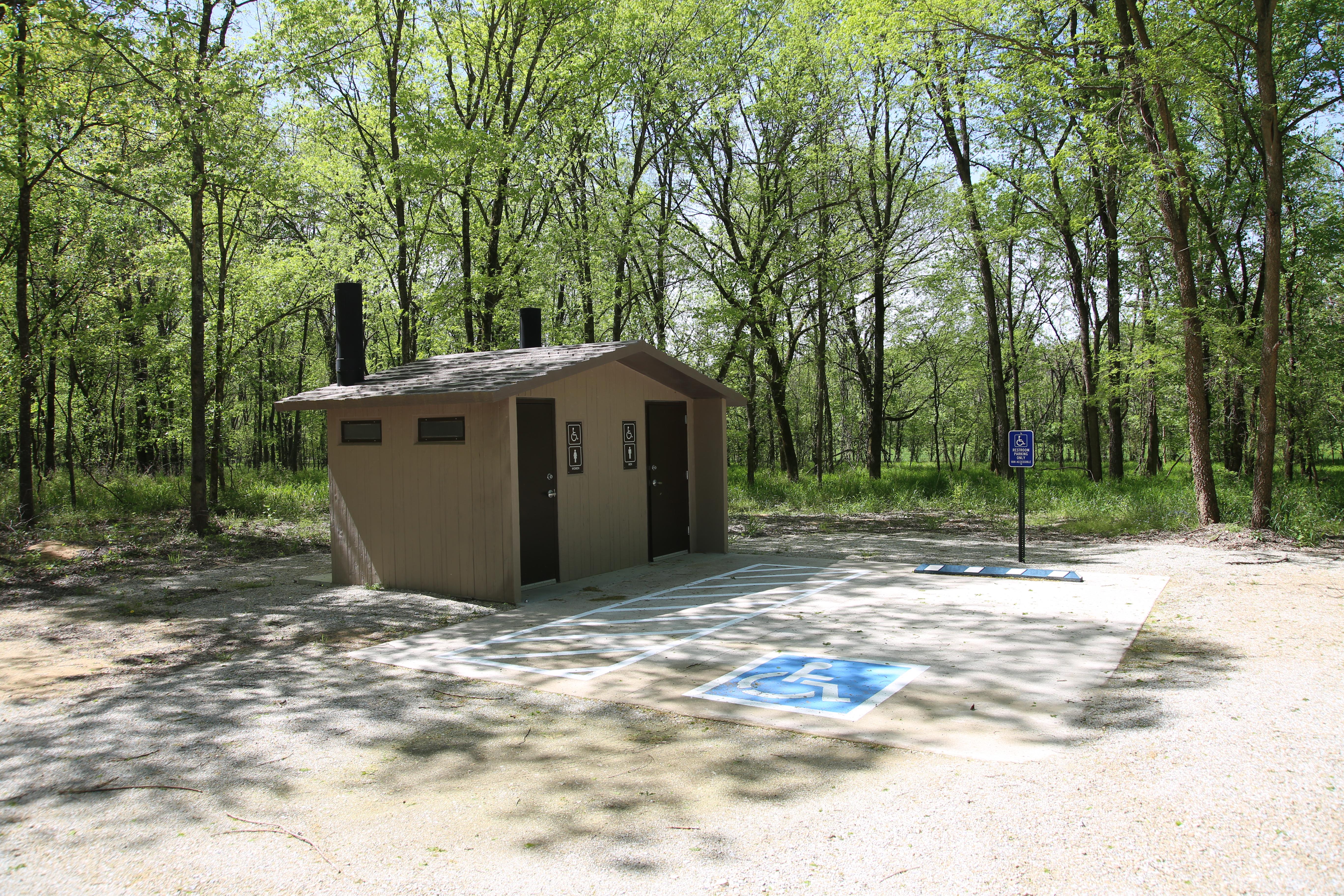 A concrete vault toilet building along the edge of a forest.