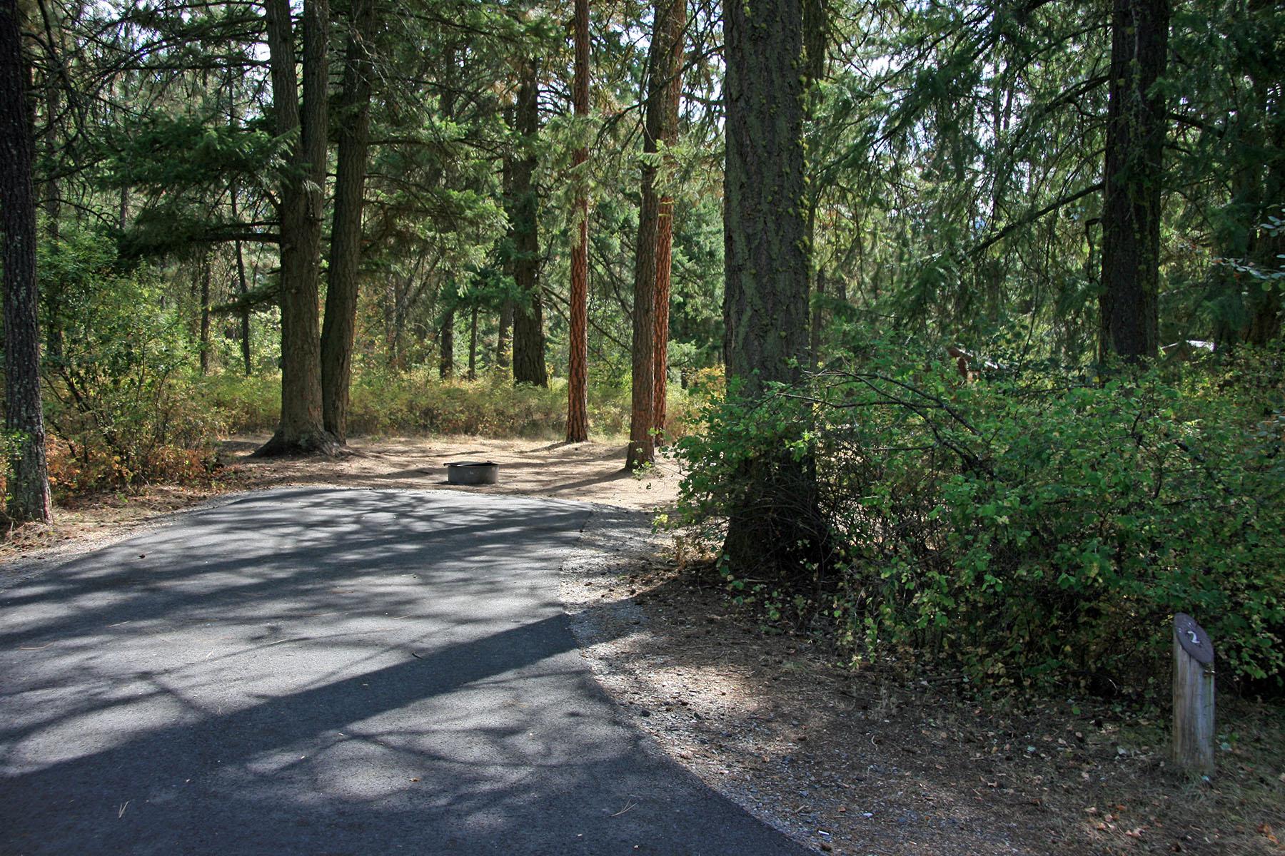 campsite with paved parking area, surrounded by trees