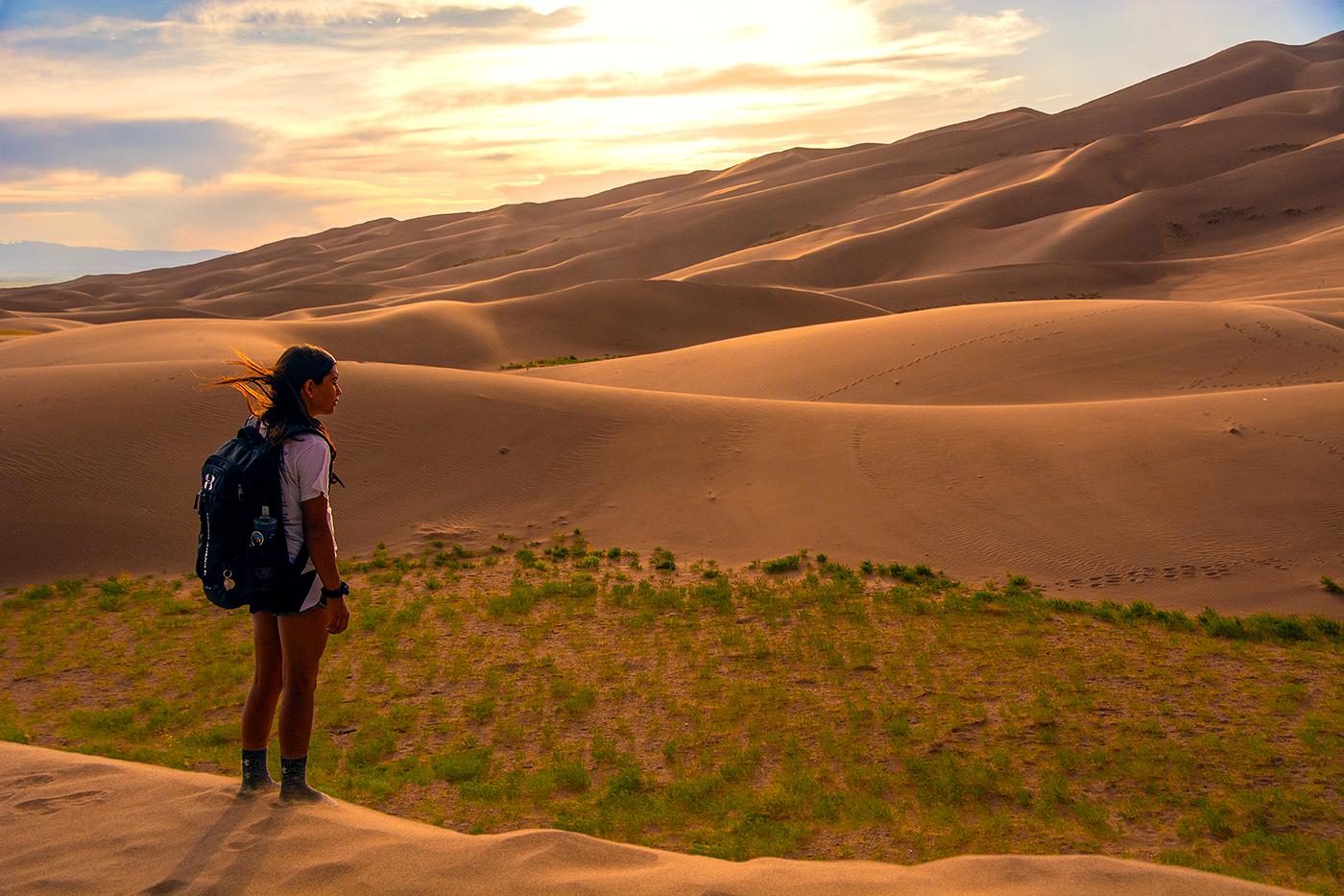 Girl with backpack viewing dunes at sunset