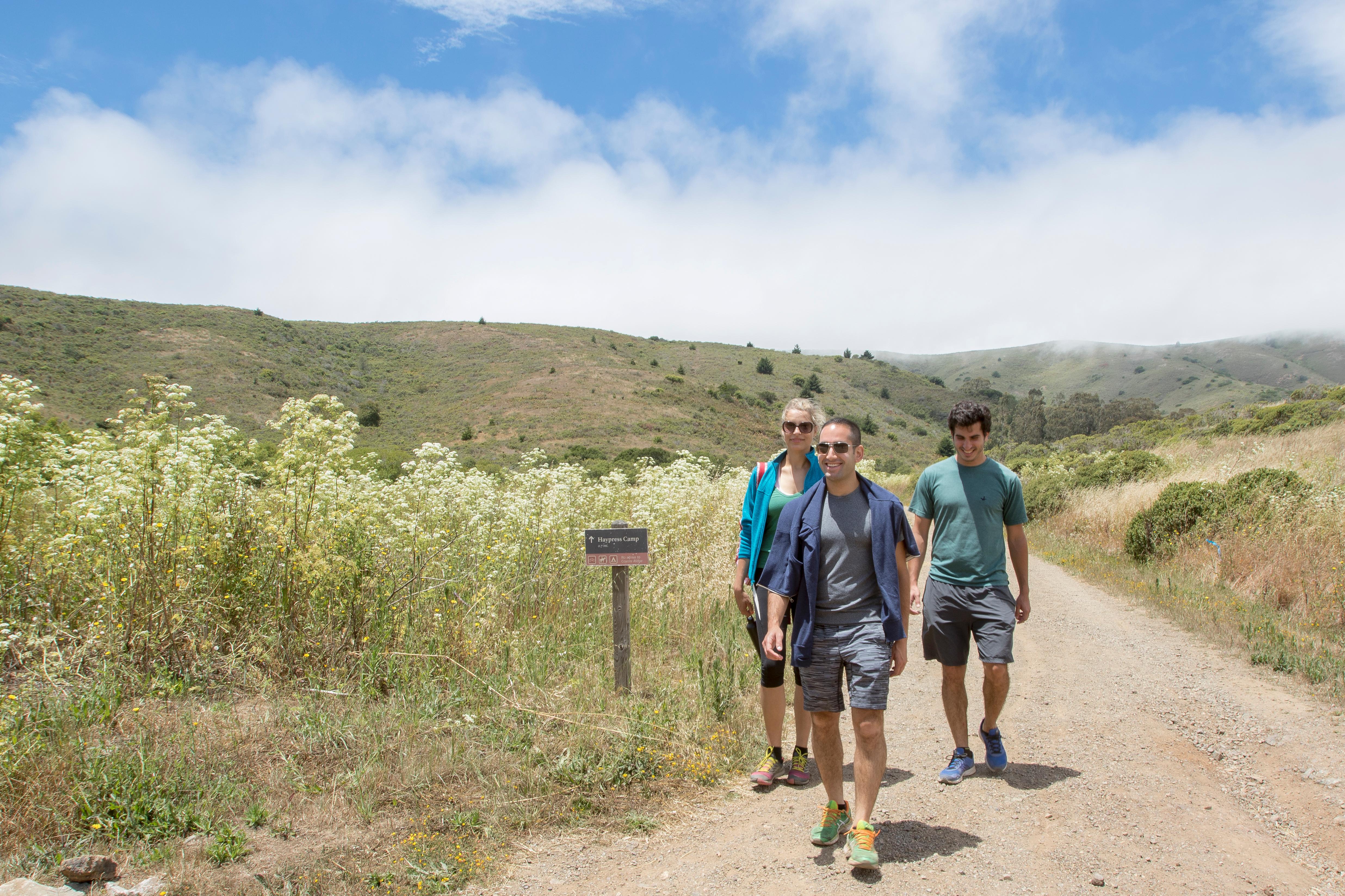 Three hikers walk along the exposed trail to Haypress Campground under cloudy, blue skies.
