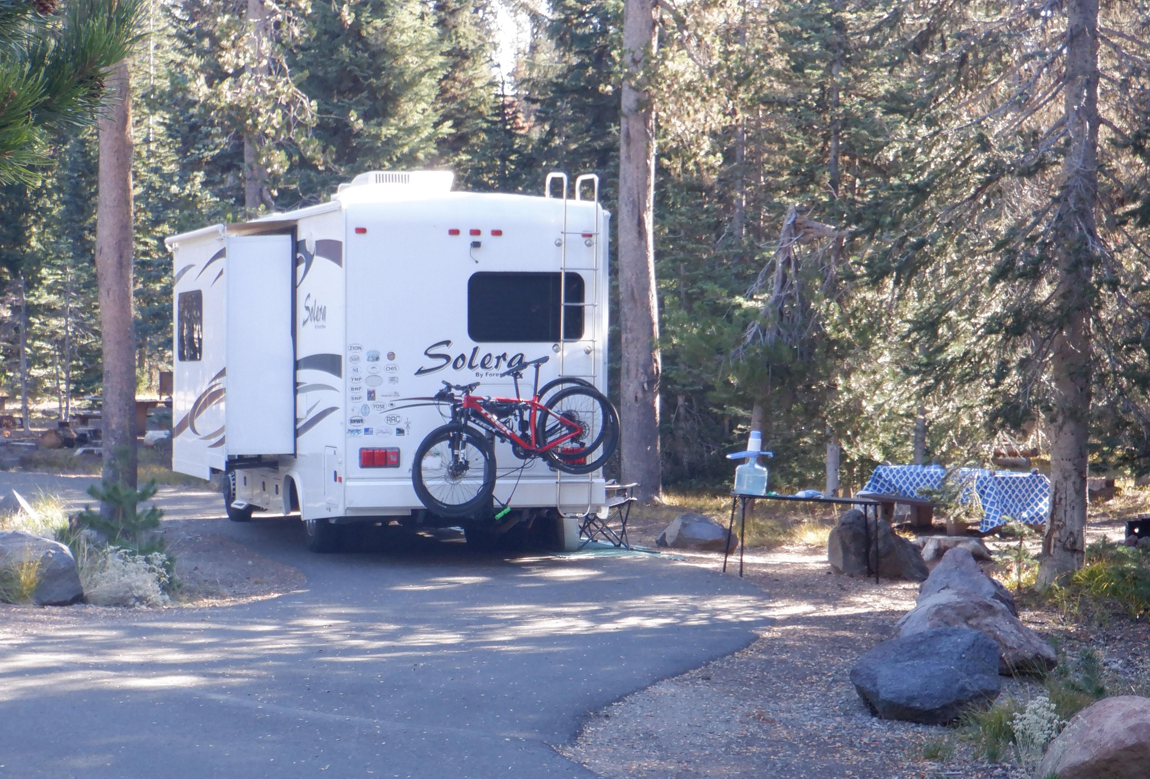 A white Solera RV with one slide out, two bikes on a rack, many stickers from national parks