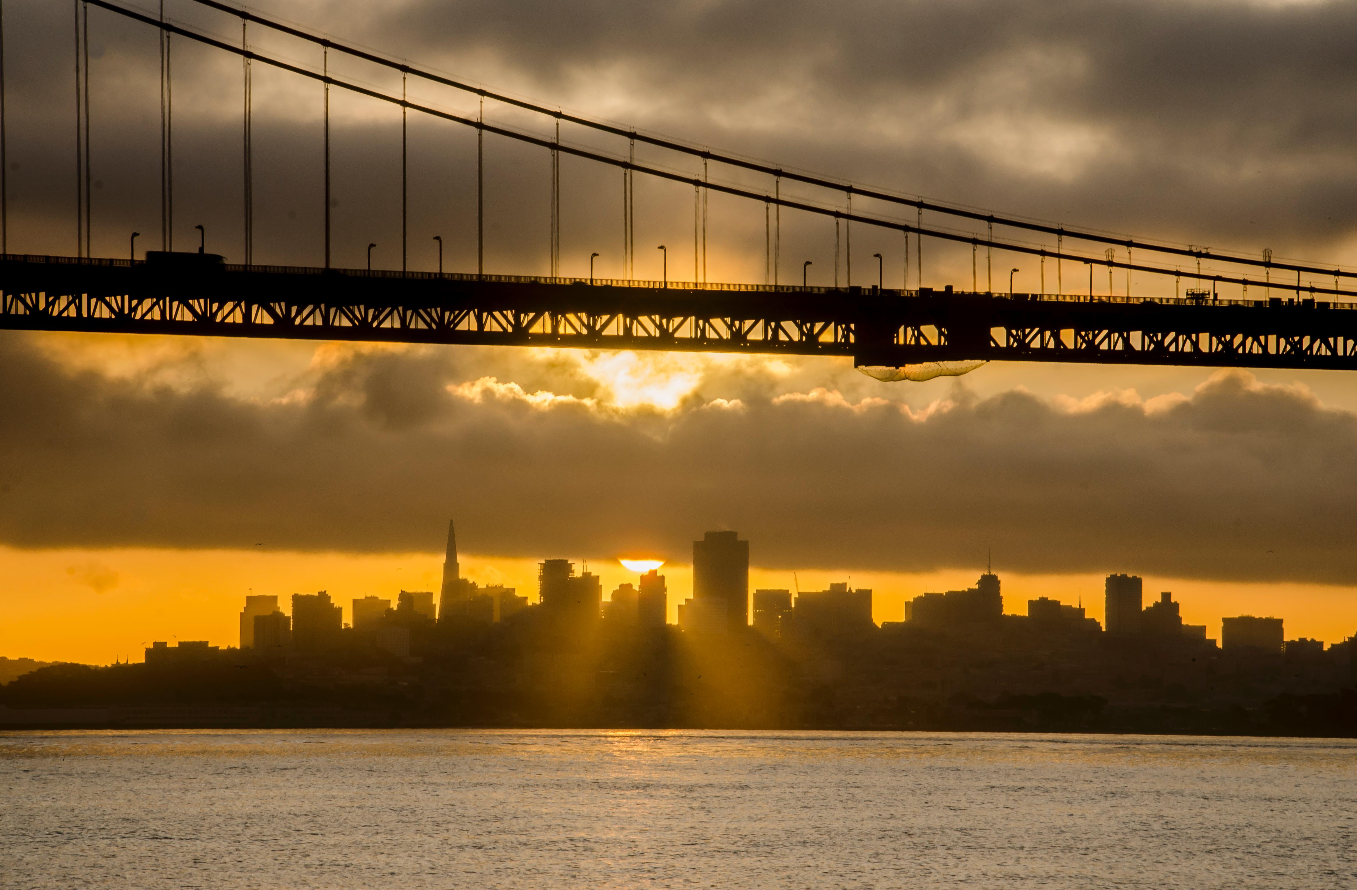 San Francisco skyline against an orange sky and cloud cover framed below the Golden Gate Bridge.