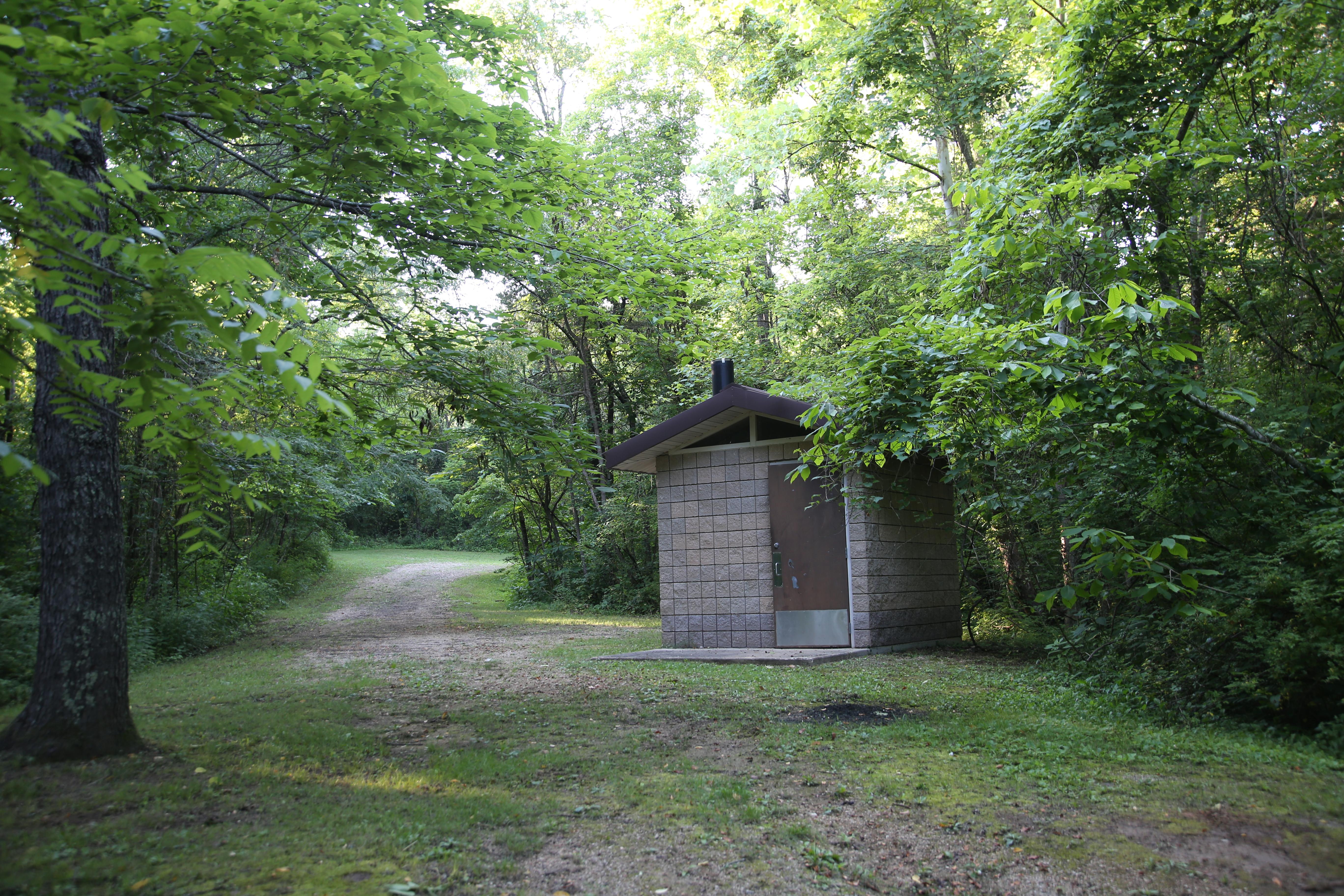 A small vault toilet building in the woods.