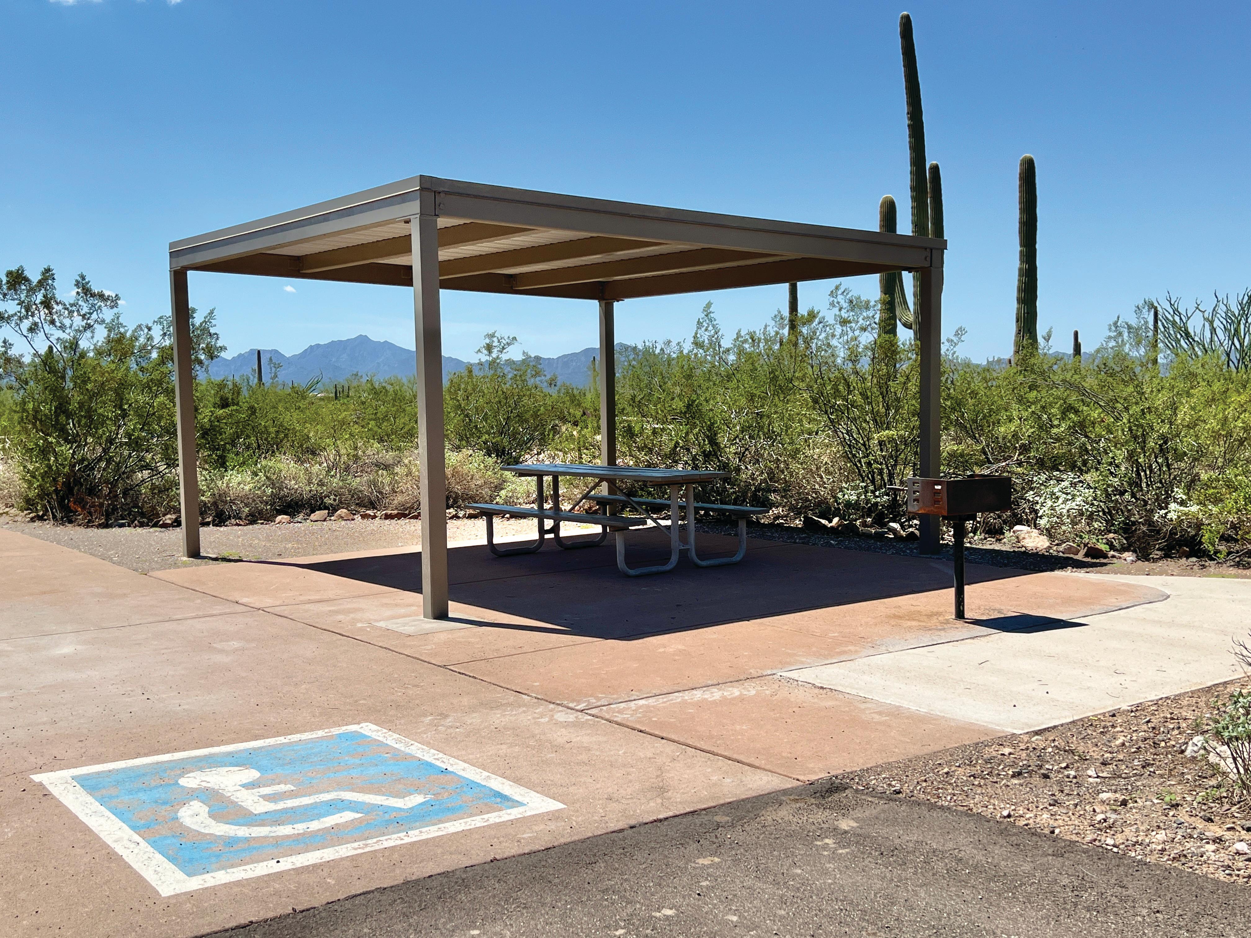 A picnic table and grill sit under a shade shelter in Twin Peaks Campground