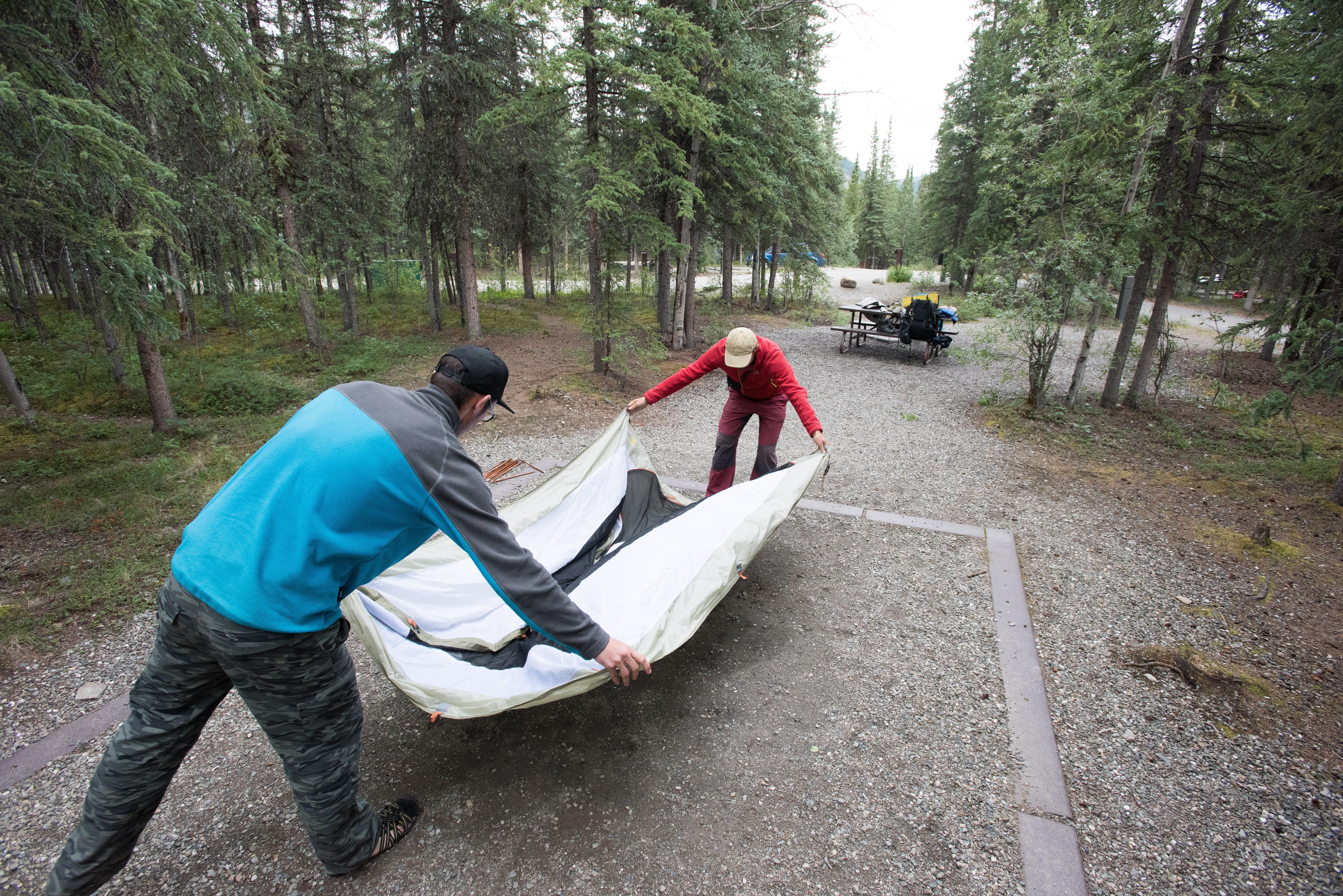 two people spreading a tent out on a gravel pad