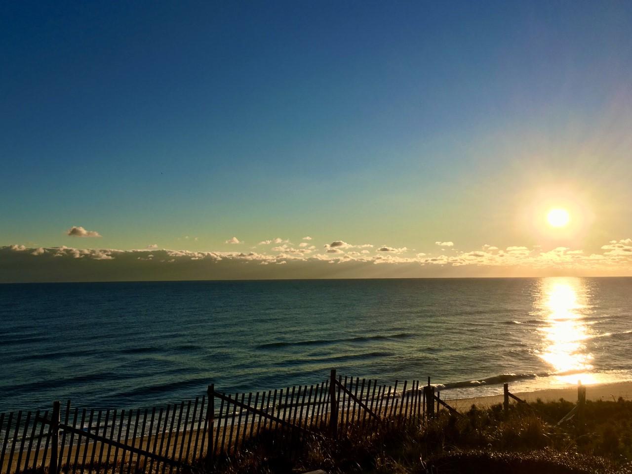 A brilliant sun rises over the ocean reflecting light on the water's surface.
