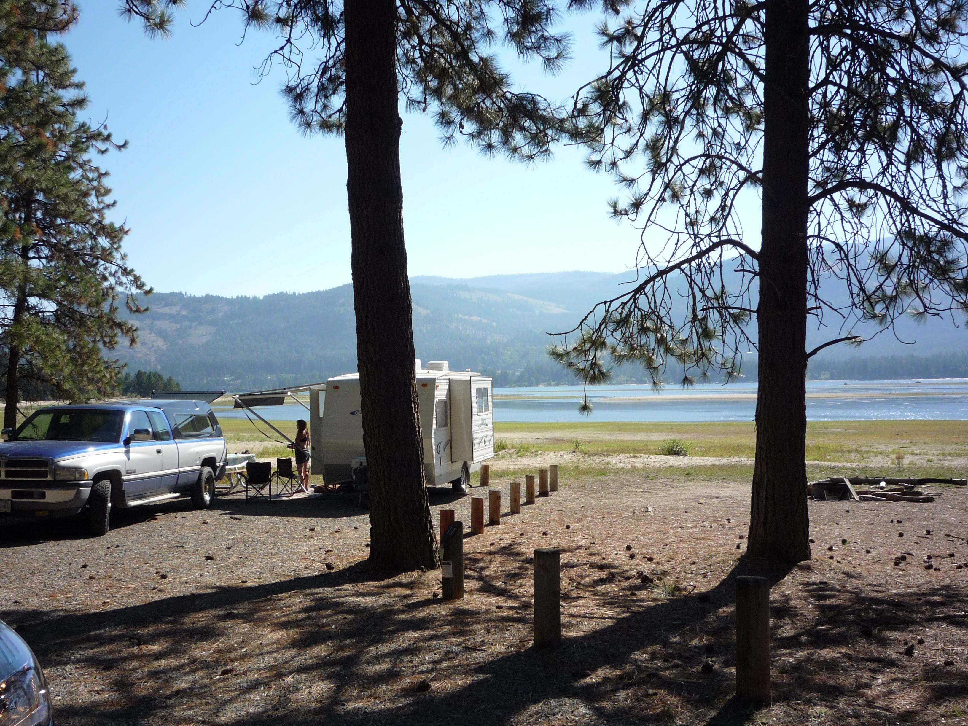 An camper trailer and truck are parked in a campsite overlooking the lake.