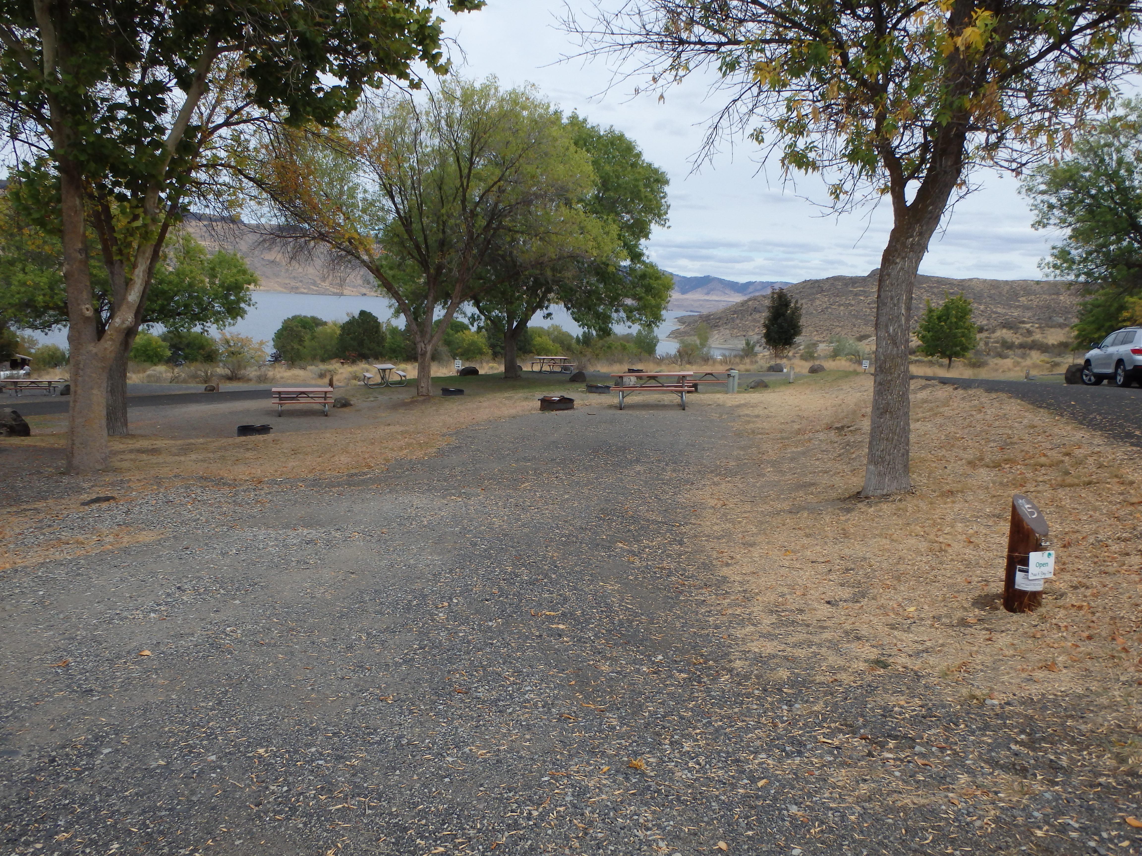 A graveled campsite pad with picnic table and fire ring adjacent.