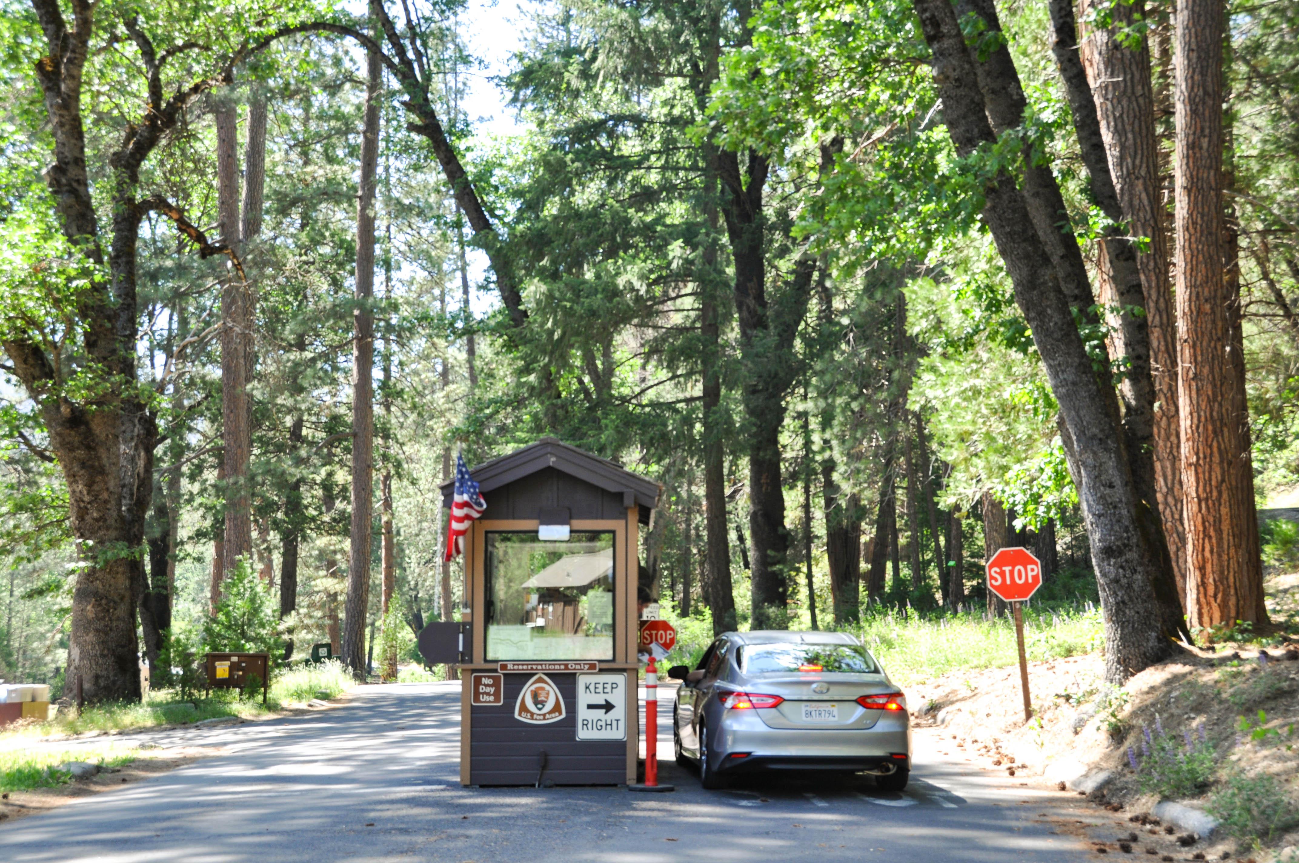 A car is stopped at a small kiosk at the entrance to a campground.