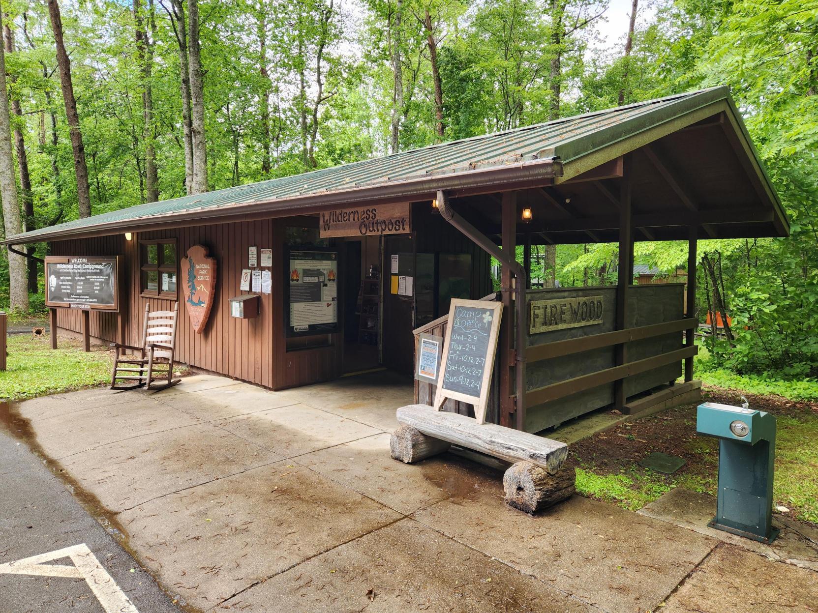 Brown building with a rocking chair and bench outside of it welcoming visitors.