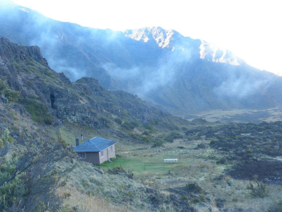 building sits at base of cliff in the distance with clouds rolling over hills in background