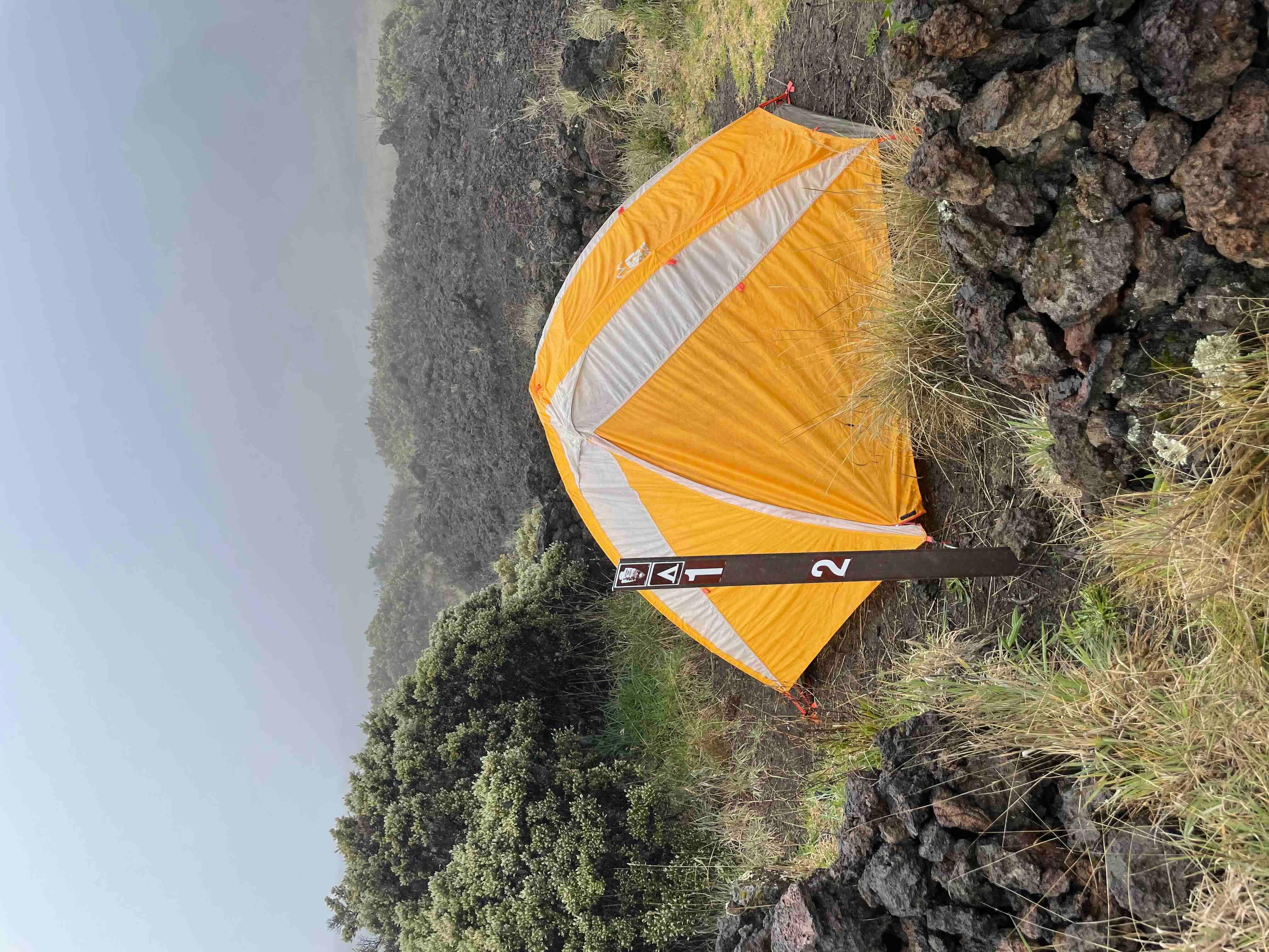 orange tent on gravel surface behind brown stake reading 1 and 2