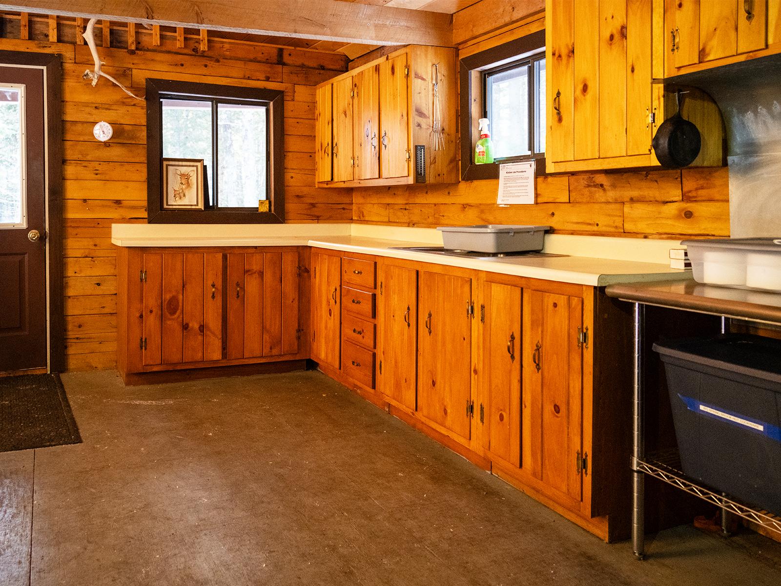 Kitchen area with a counter, cabinets, and sink. A door and windows bring light into the hut.
