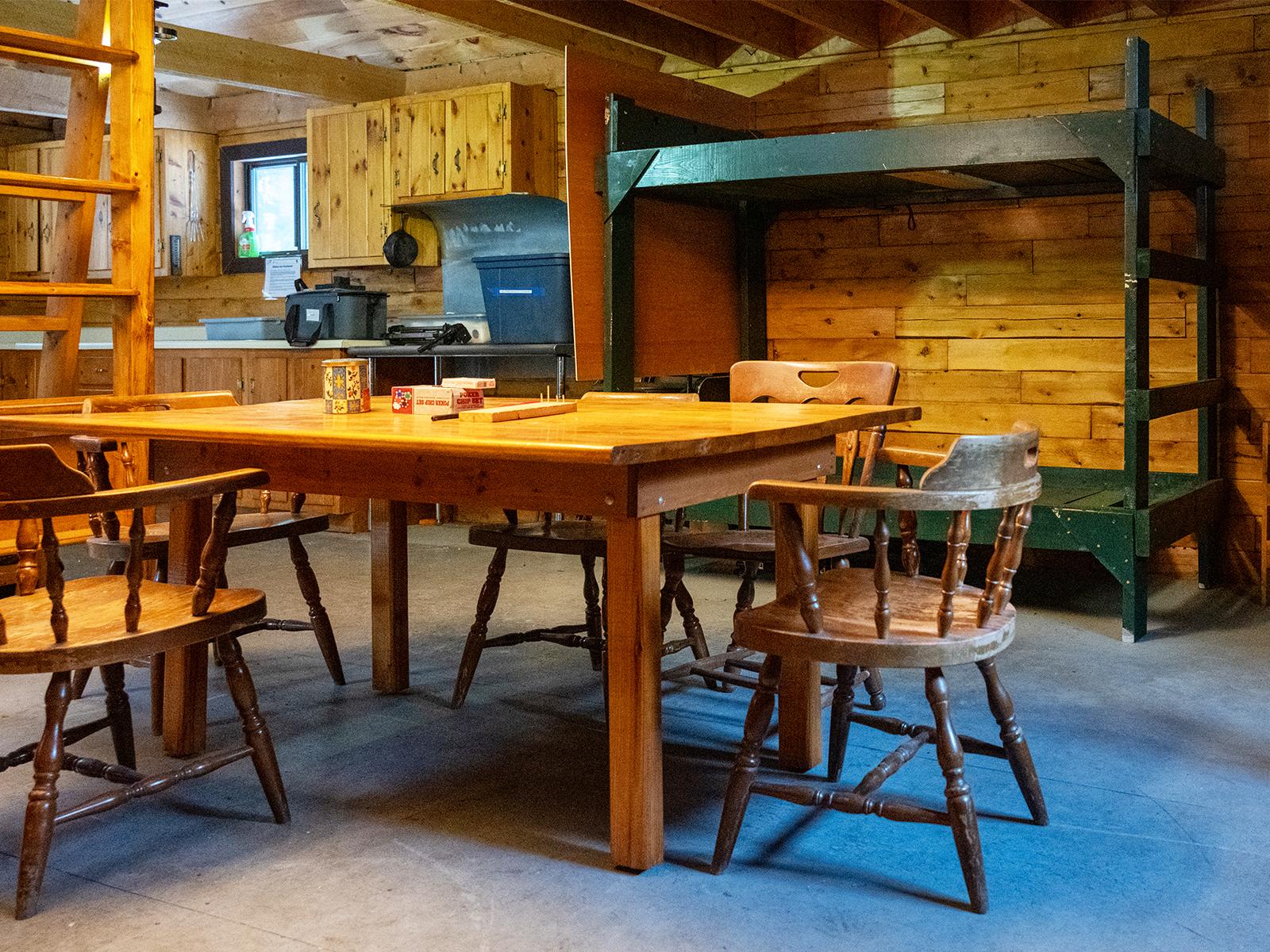Wooden dining table with card games and green bunk beds behind. Kitchen is in the background