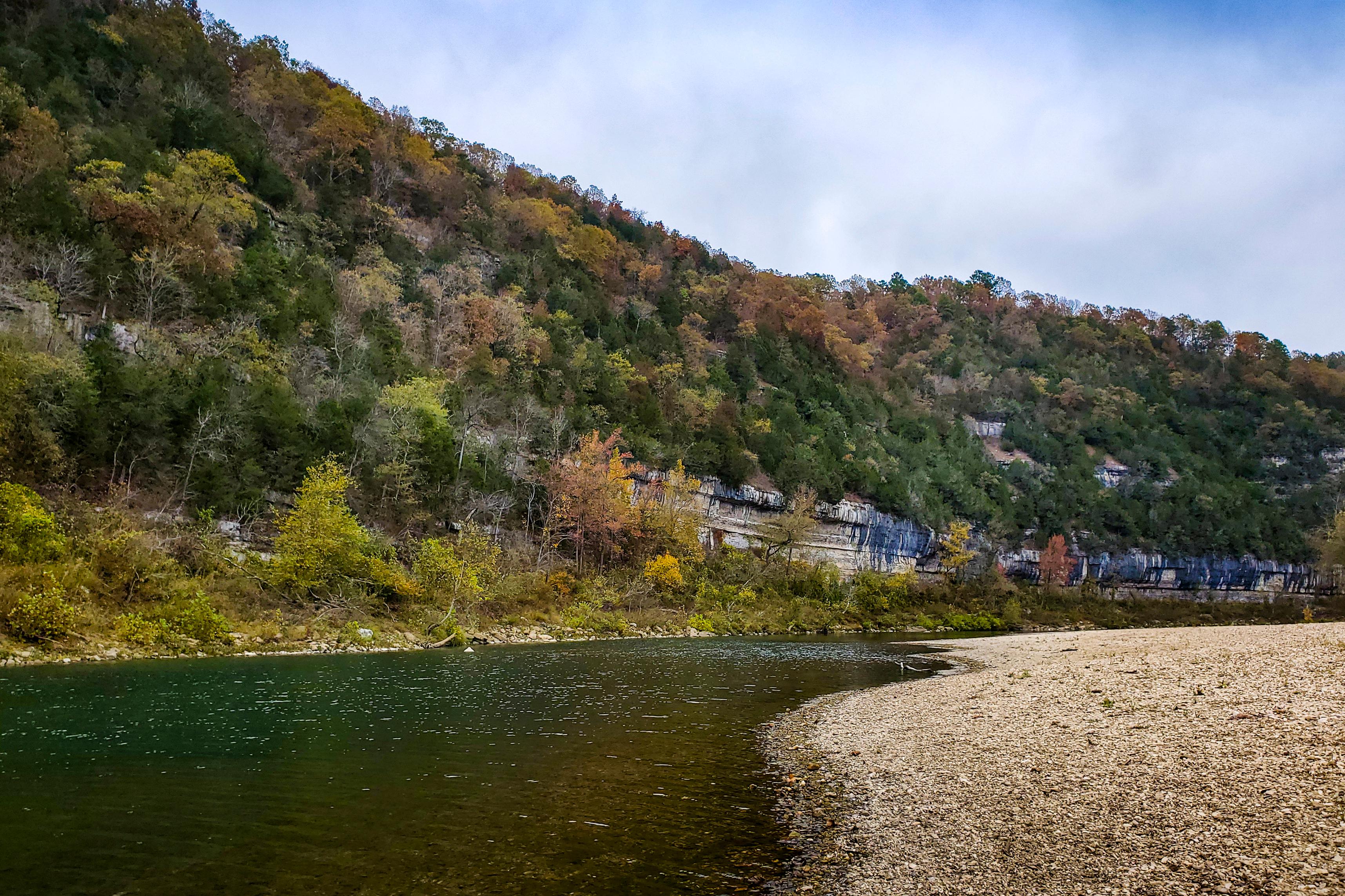 River and gravel bar with a cliff face covered in trees with yellow leaves..