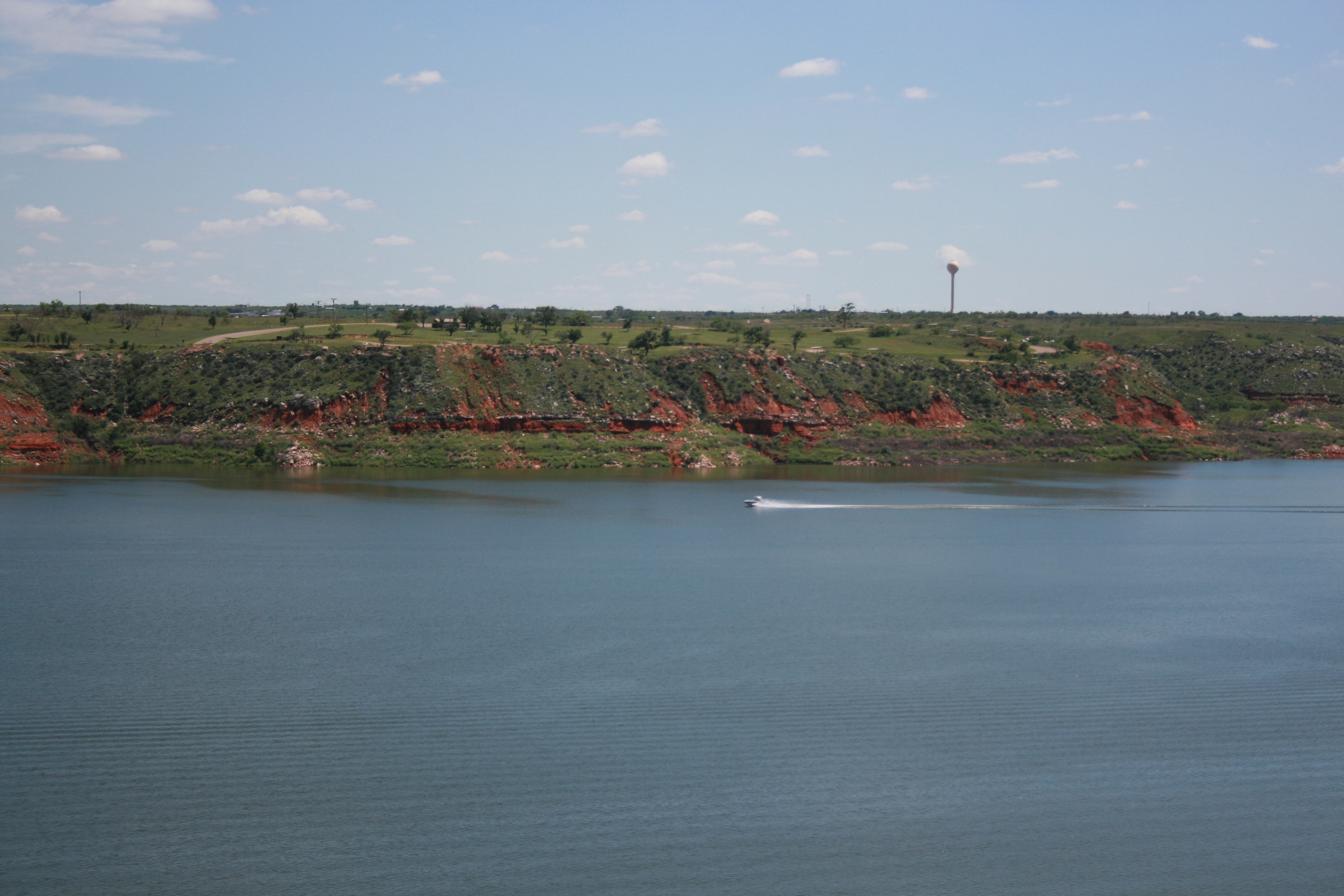 A boat travels across Lake Meredith on a sunny day. The lake is light blue.